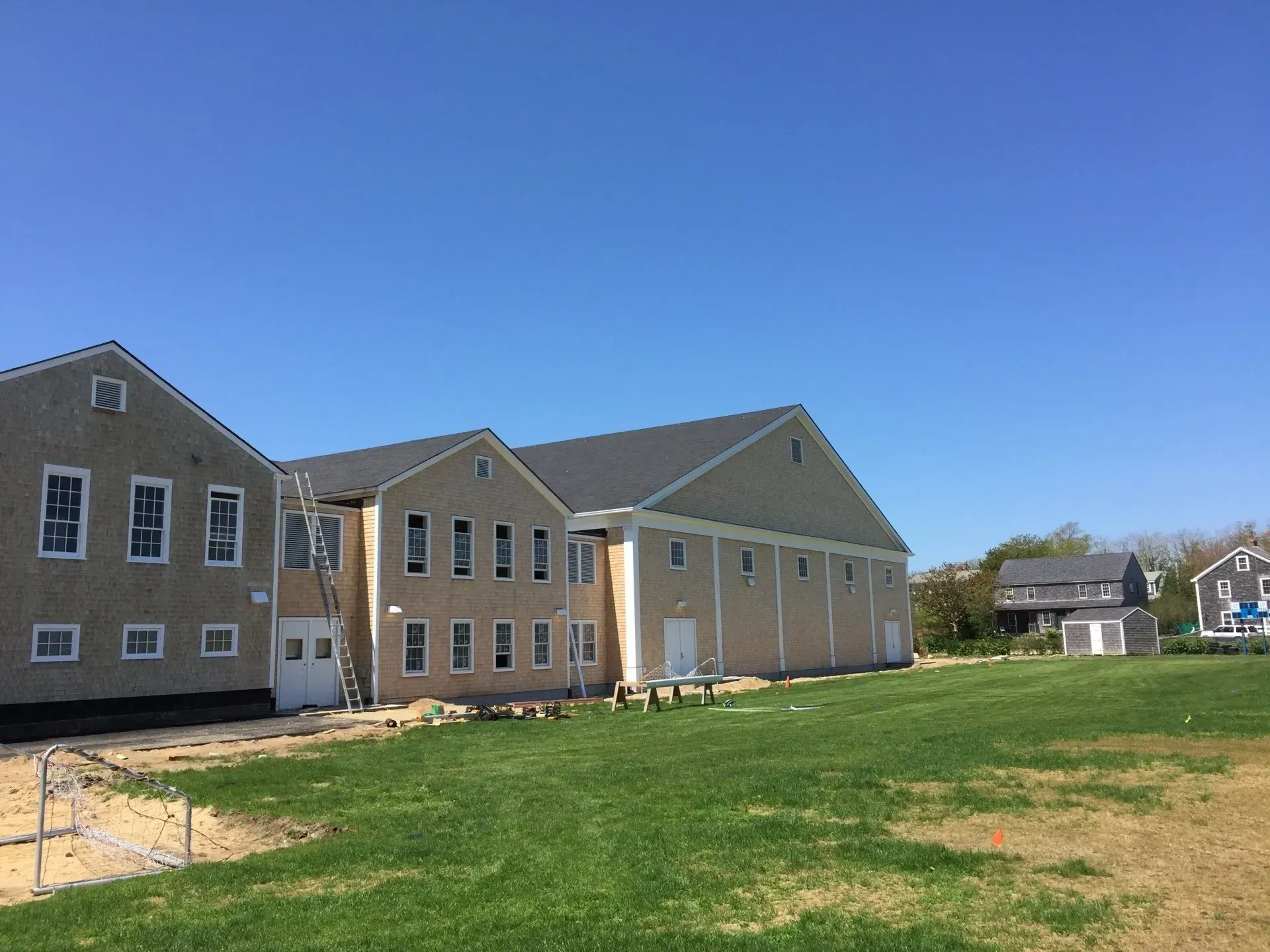 Light-colored building under construction on a grassy lot, with a clear blue sky.