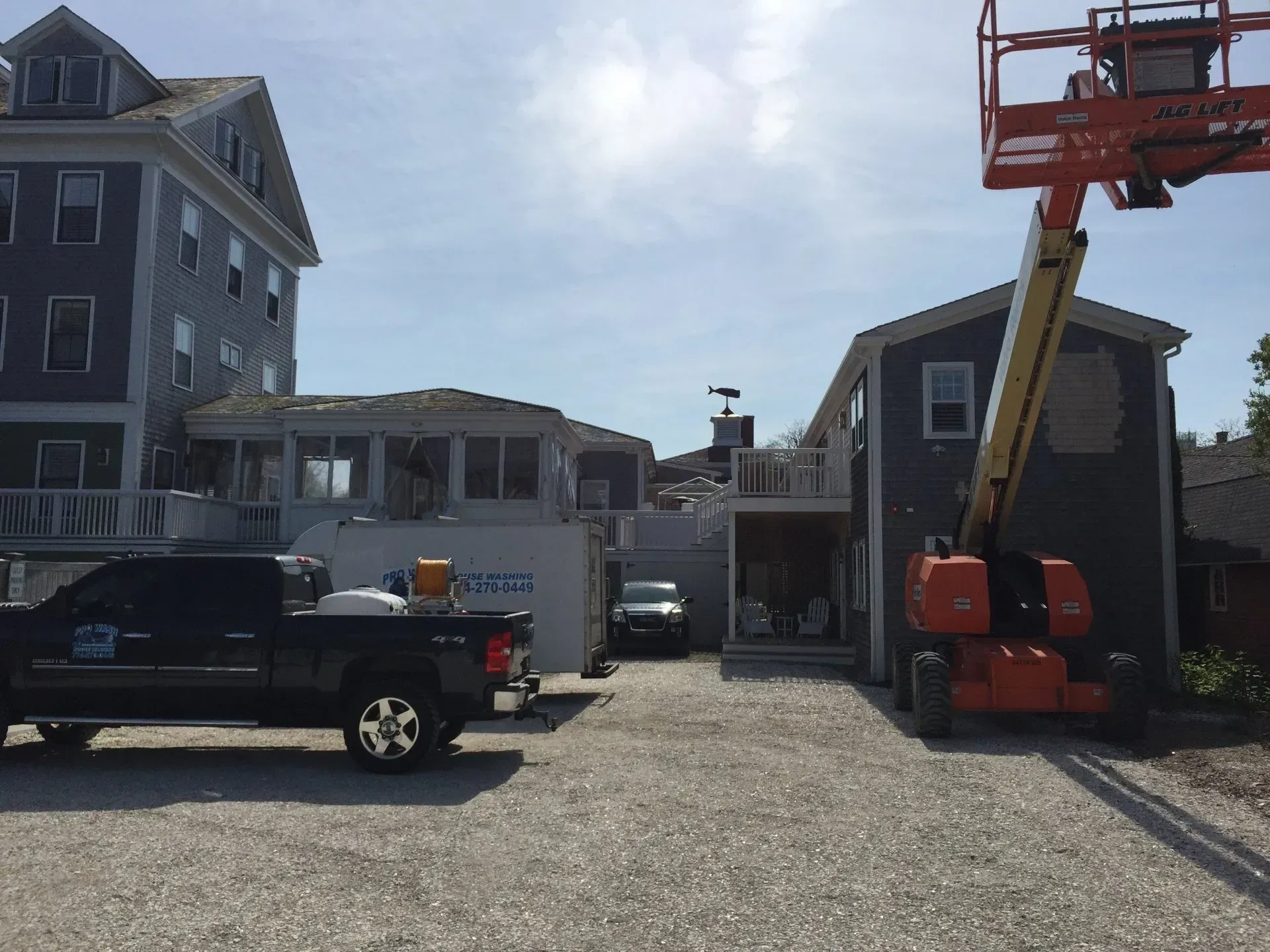 Construction site: Truck, lift, and buildings under renovation on a gravel lot under a sunny sky.