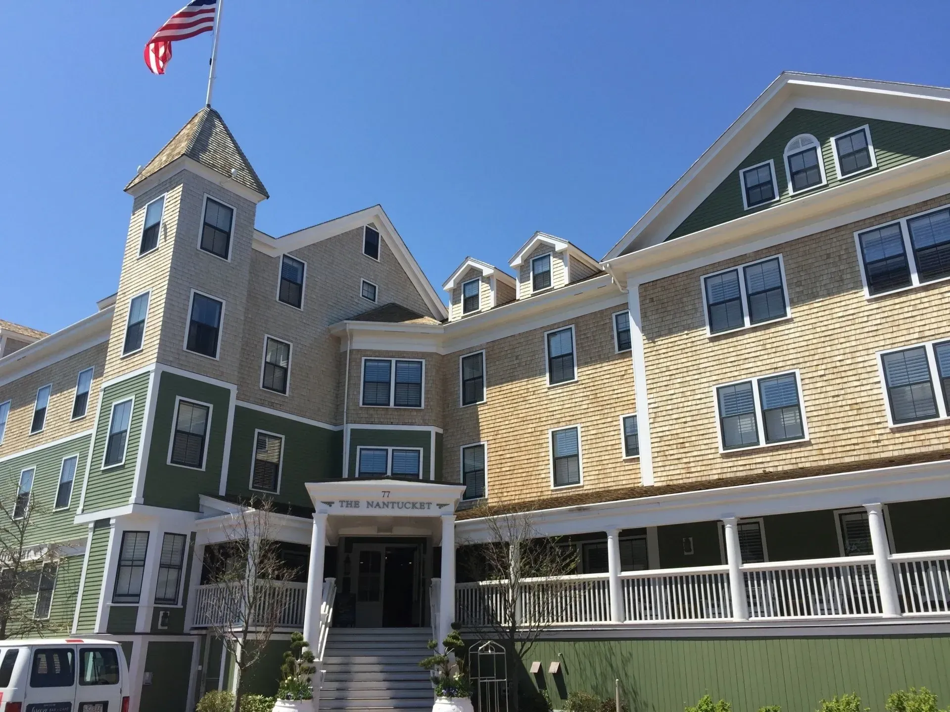 Large light-colored building with green trim, porch, and a tower with a waving American flag.