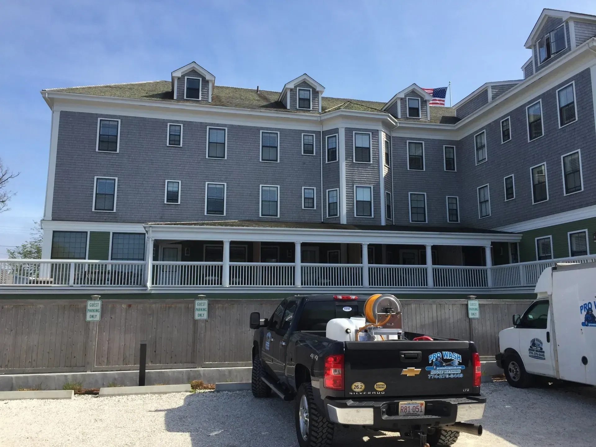 Gray hotel with multiple windows, parked truck with spraying equipment in front. Blue sky.