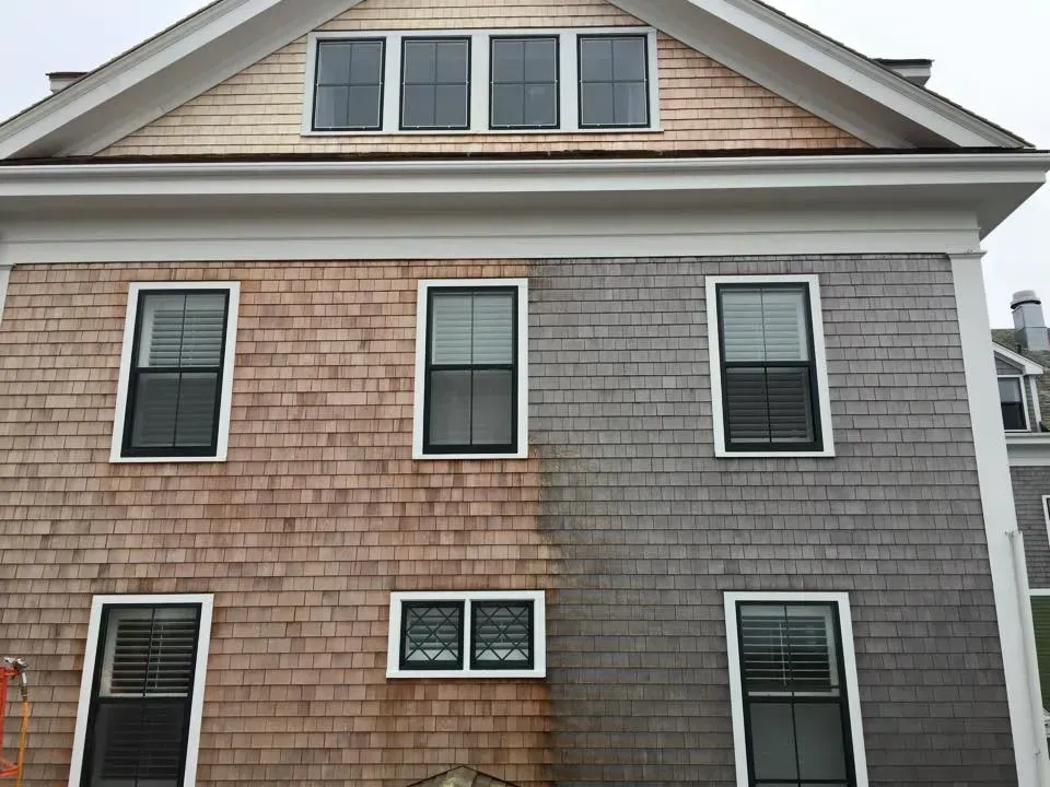 Half of a wooden shingled house cleaned, showing the contrast between dirty and freshly cleaned sides.