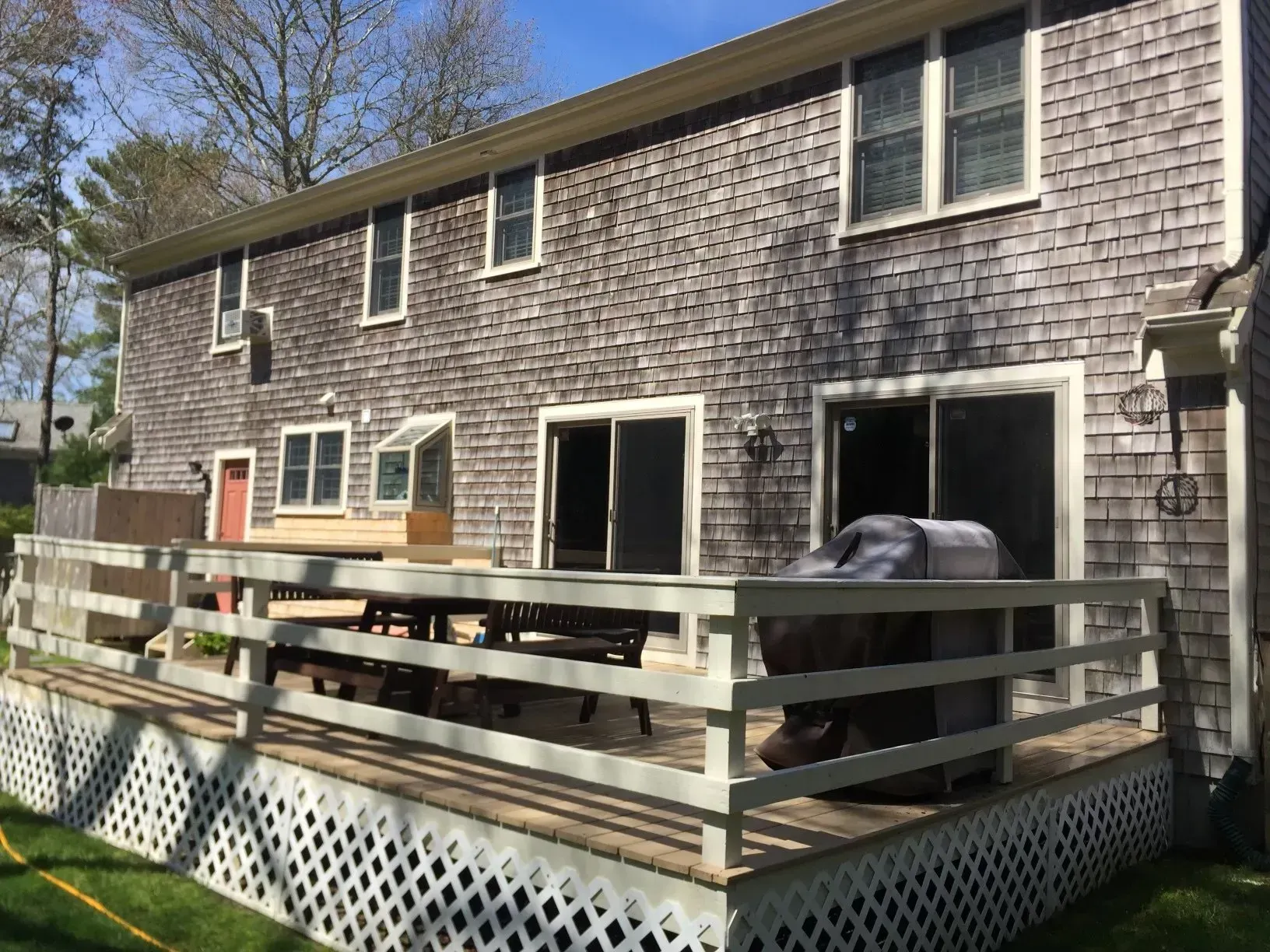 Back of a two-story wooden shingle house with a deck. The deck has a white railing, and sliding glass doors.
