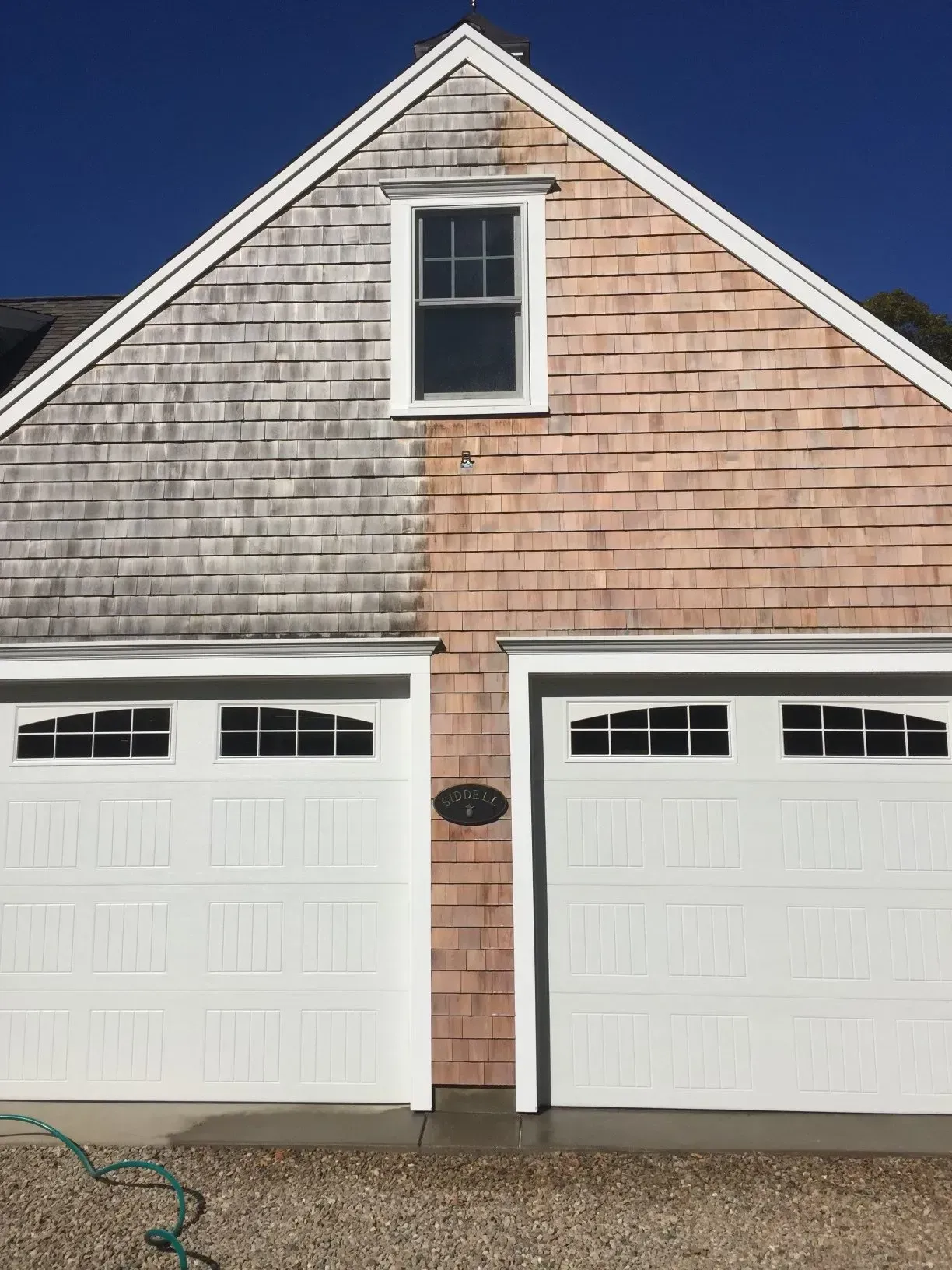 Garage with wooden shingles, half cleaned, showing before-and-after effect of a cleaning. White doors.