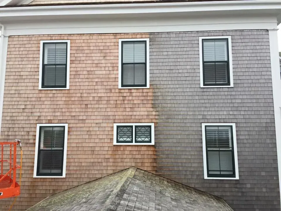 Side of building being cleaned, showing difference between dirty, brown shingles and clean, gray shingles.