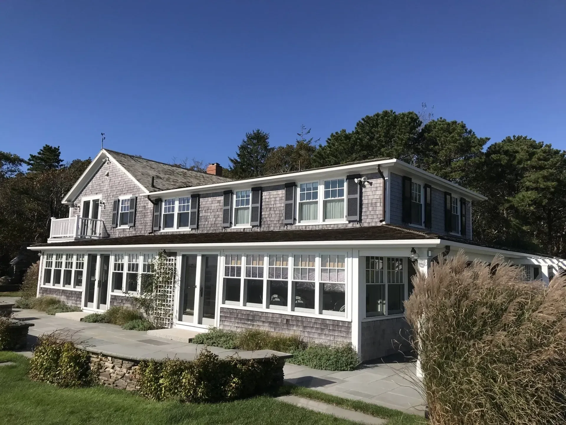 Two-story weathered gray house with a porch and multiple windows, under a blue sky.