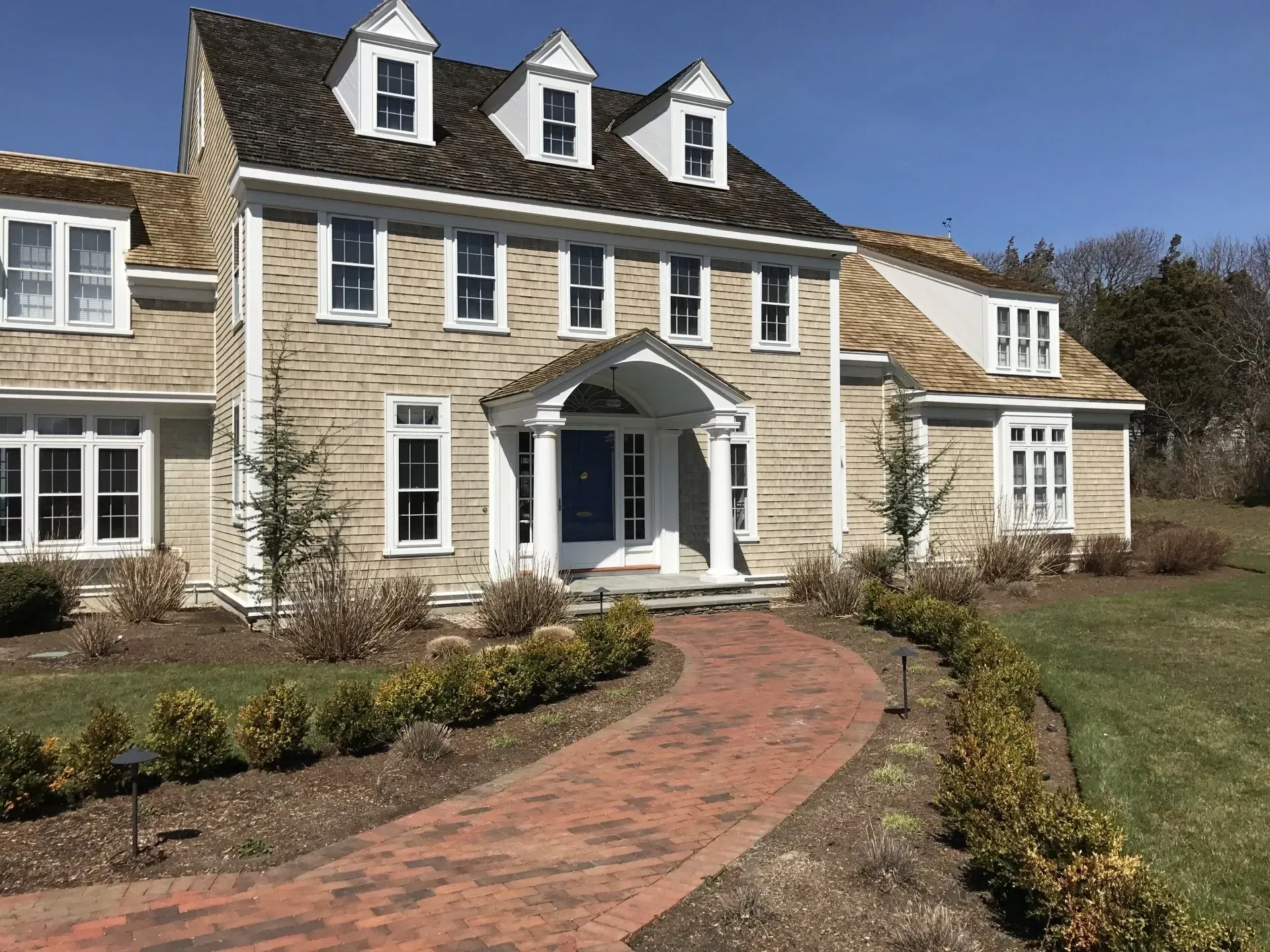 Beige house with brick pathway leading to a blue front door. Three dormers.