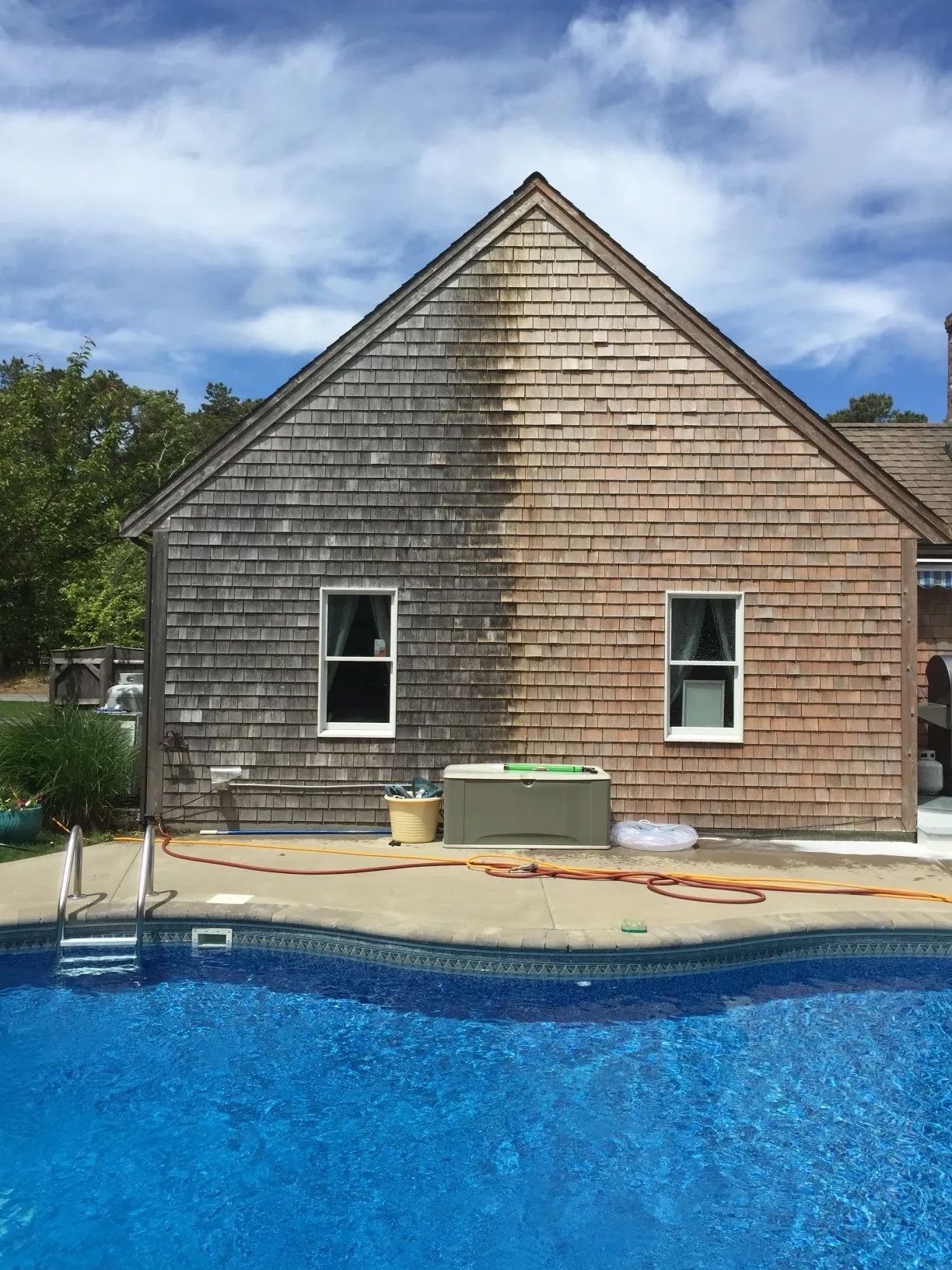 House siding being pressure washed; half clean, half dirty, beside a pool.