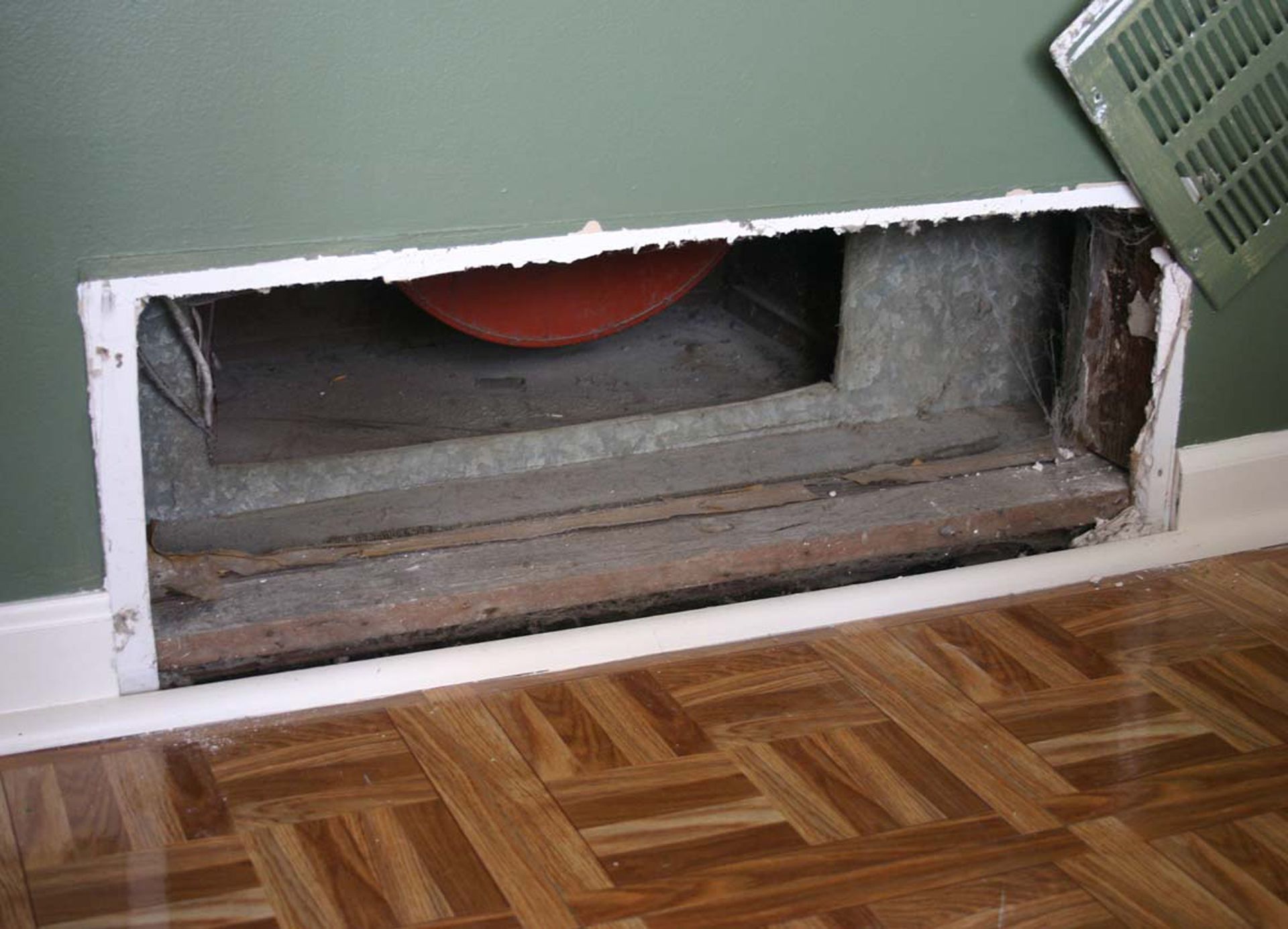 Open air vent in wall, missing cover, showing interior with a red disc inside.