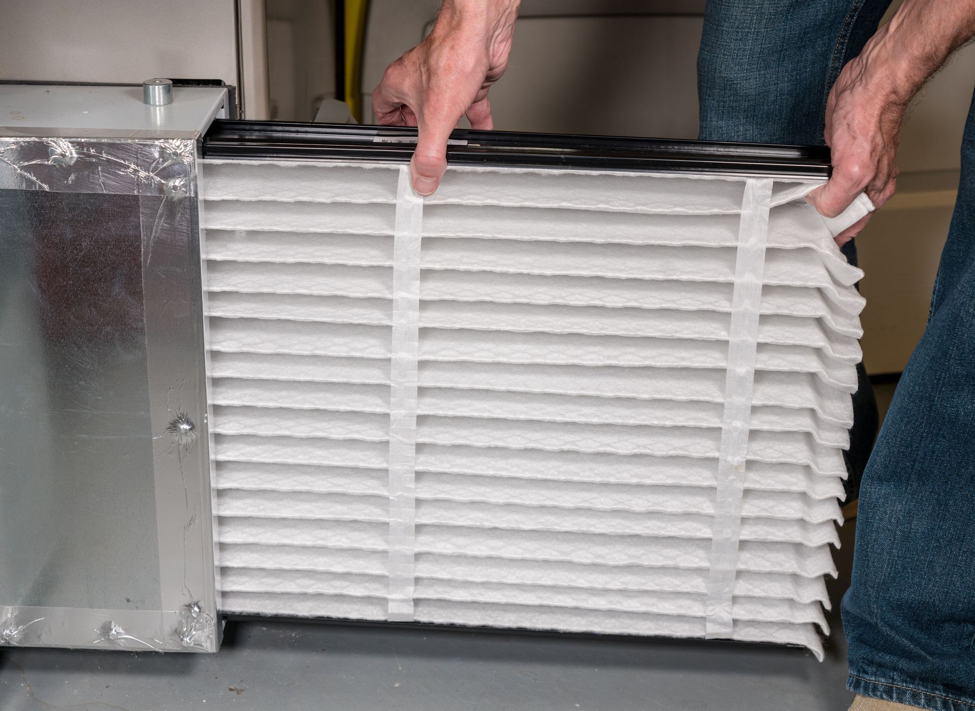 Person replacing a pleated air filter in a furnace, with hands holding the filter.