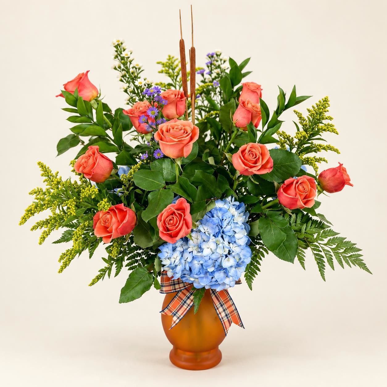 Coral roses and blue hydrangeas in a terracotta vase with greenery and a plaid ribbon bow