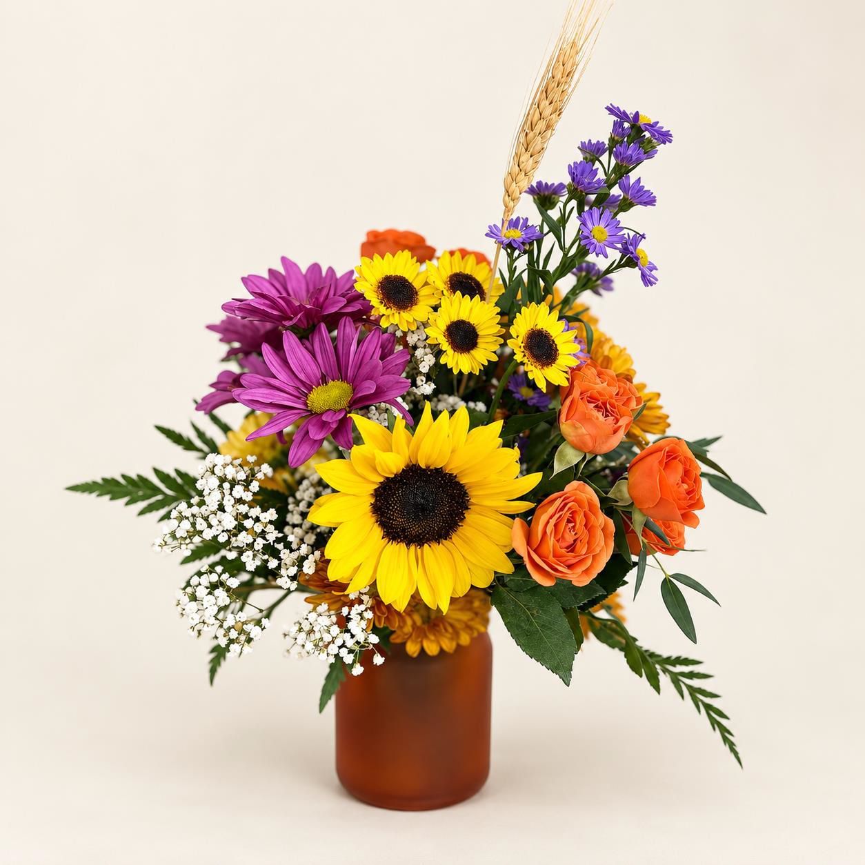 Colorful mixed bouquet with sunflowers, purple daisies, orange roses, and baby's breath in a brown vase