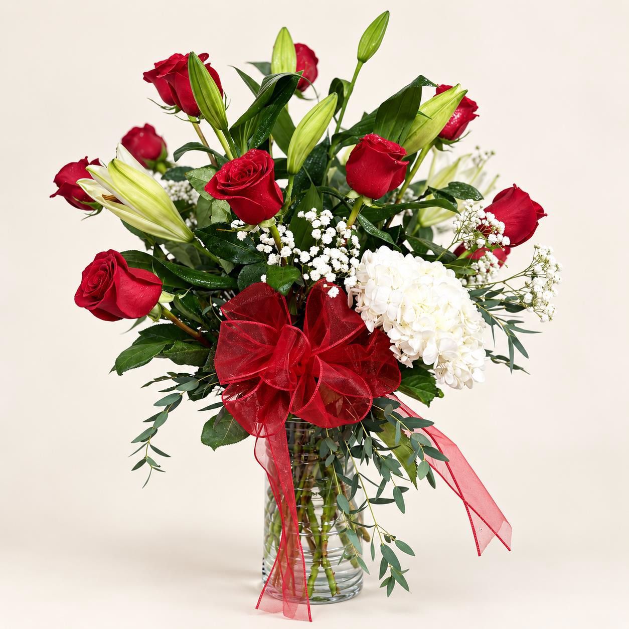Bouquet of red roses, white lilies, and baby's breath with red ribbon in a glass vase