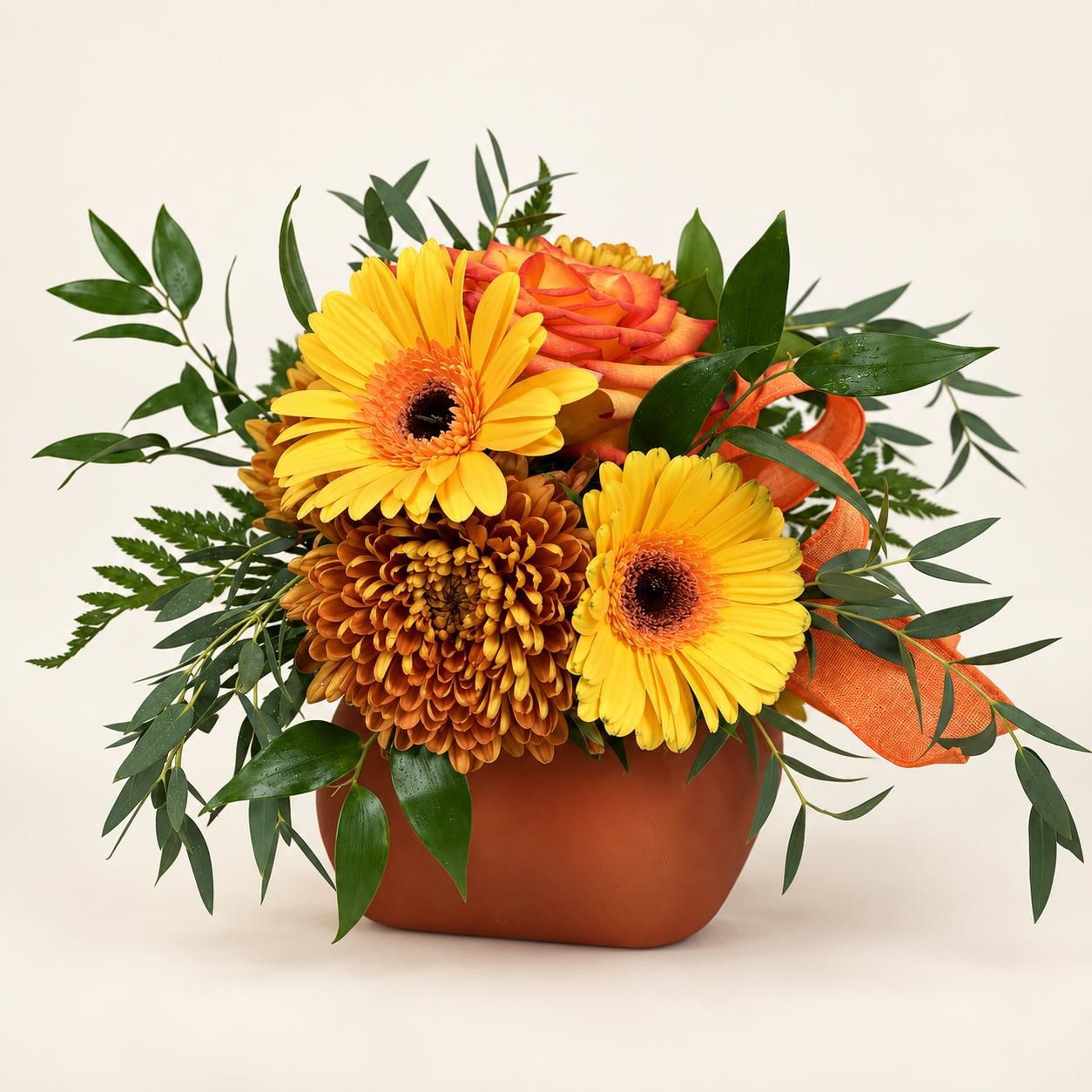 Mixed orange and yellow flowers arranged in a terracotta pot with green leaves