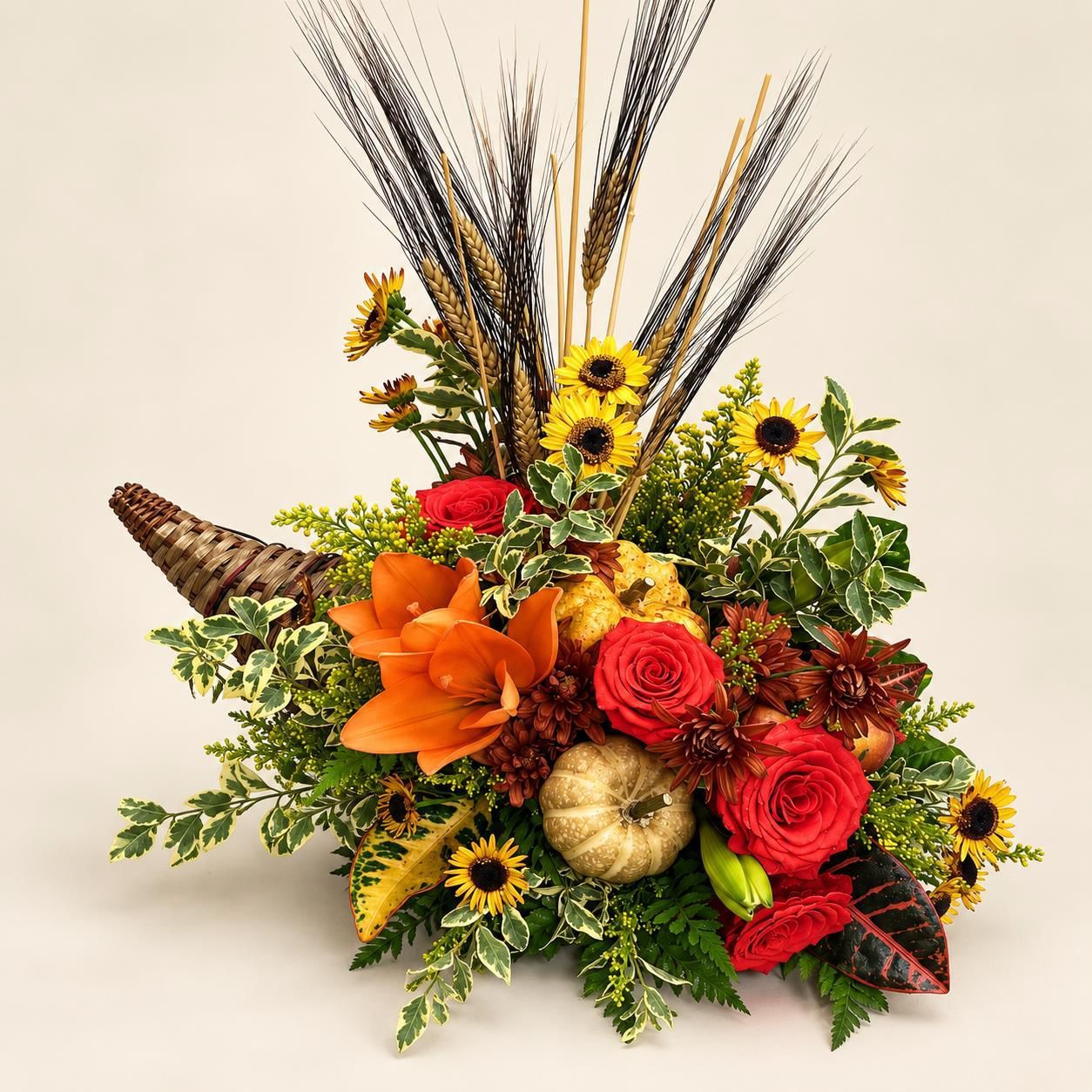 Autumn floral arrangement with orange lilies, red roses, sunflowers, and dried wheat in a basket
