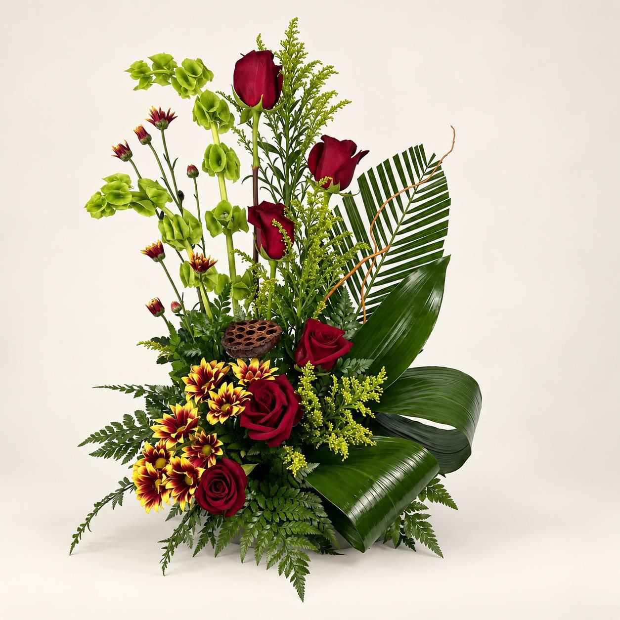 Red and yellow floral arrangement with roses, greenery, and large tropical leaves on a white background