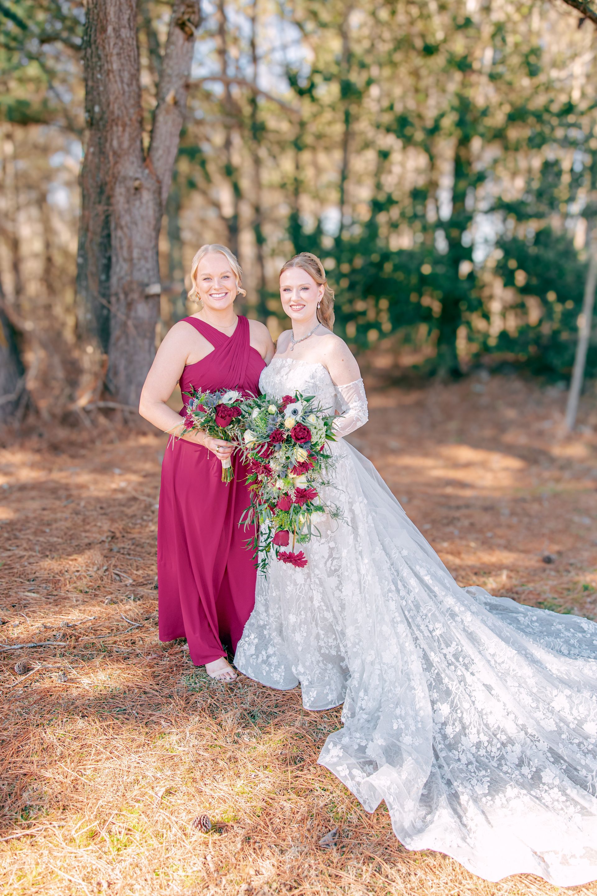 Two people in dresses posing outdoors in a wooded area, holding a cascading bouquet.