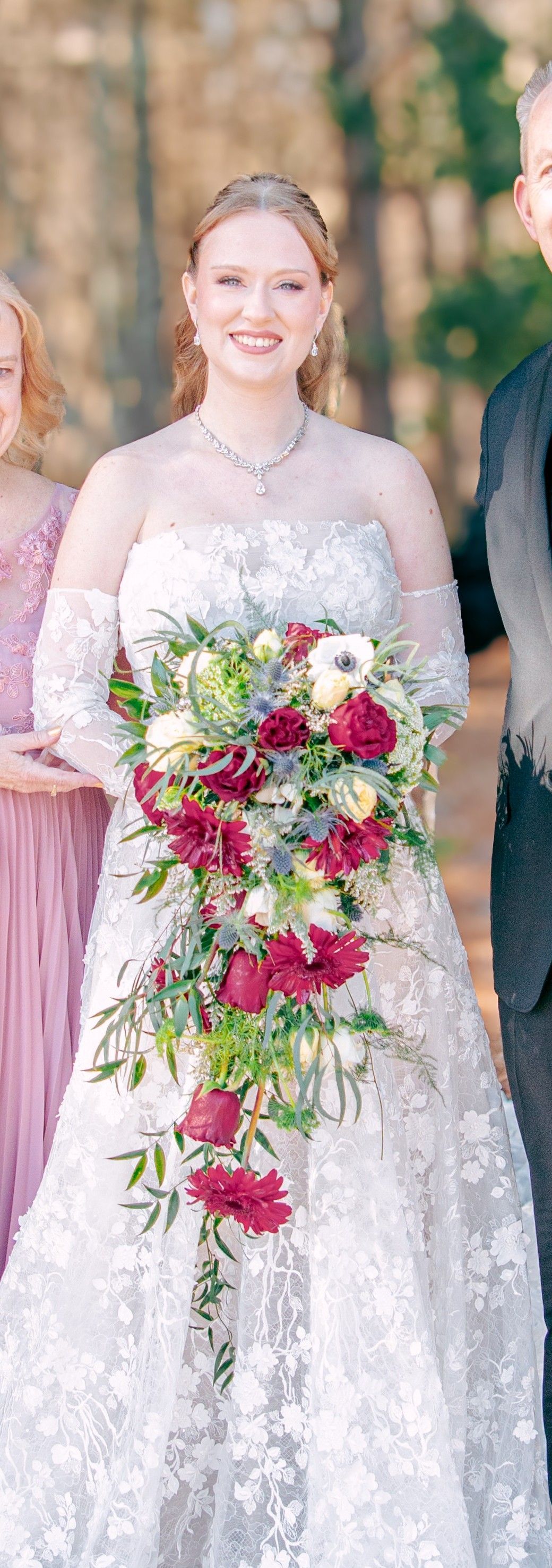 Bride in a lace gown holding a colorful cascading bouquet outdoors on a wedding day