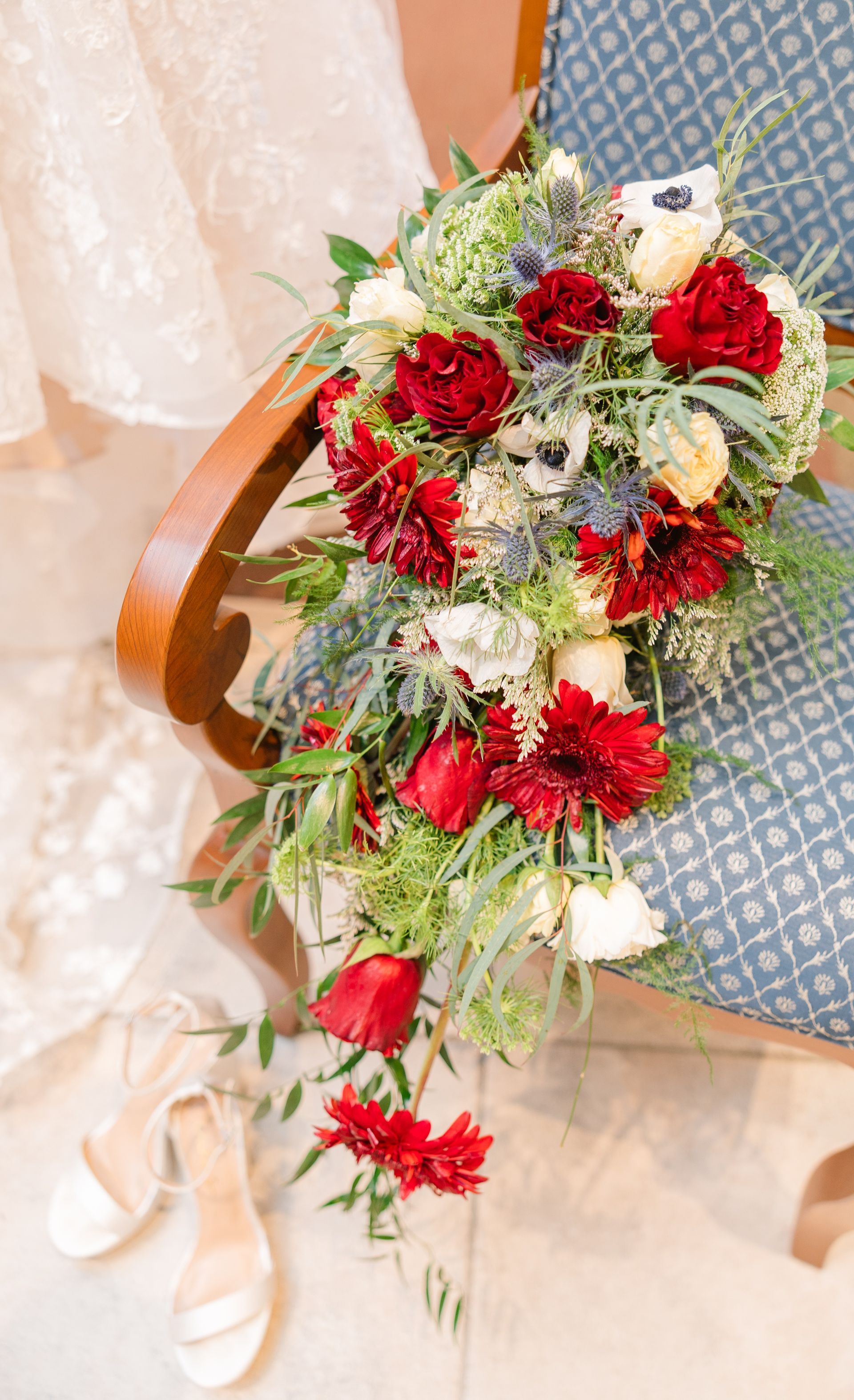 Red and white floral bouquet cascading over a chair beside a person in a pale dress and ballet flats