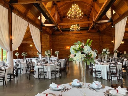 Rustic wedding reception hall with chandeliers, white-draped tables, and floral centerpieces