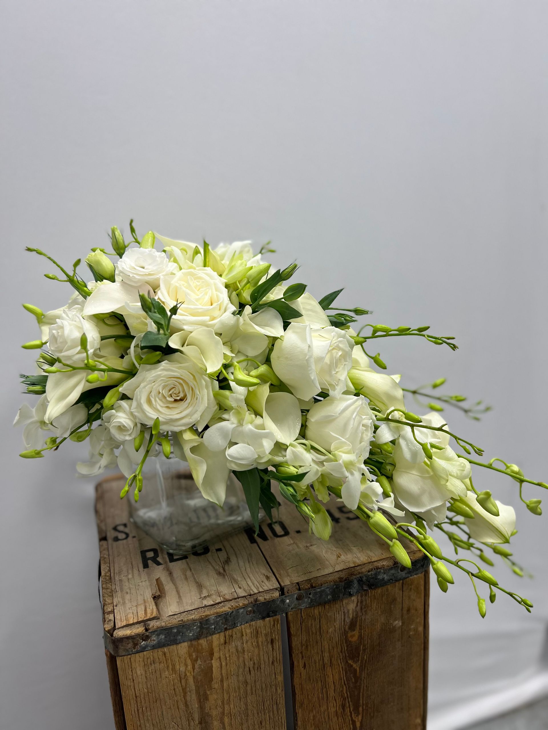 White rose and lily floral arrangement on a wooden crate against a gray backdrop