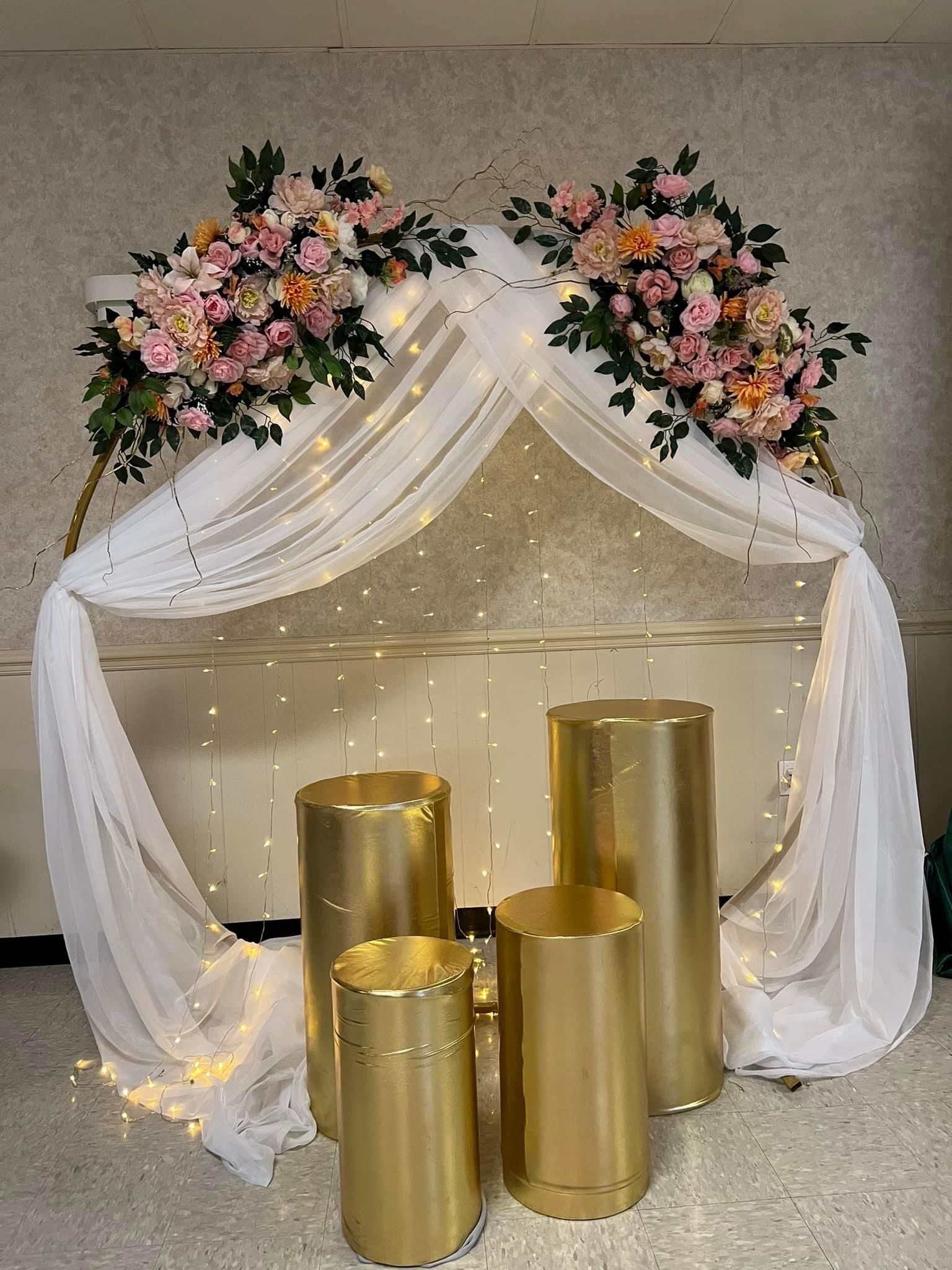 Gold pedestal display with white draped canopy and pastel floral arrangements on top