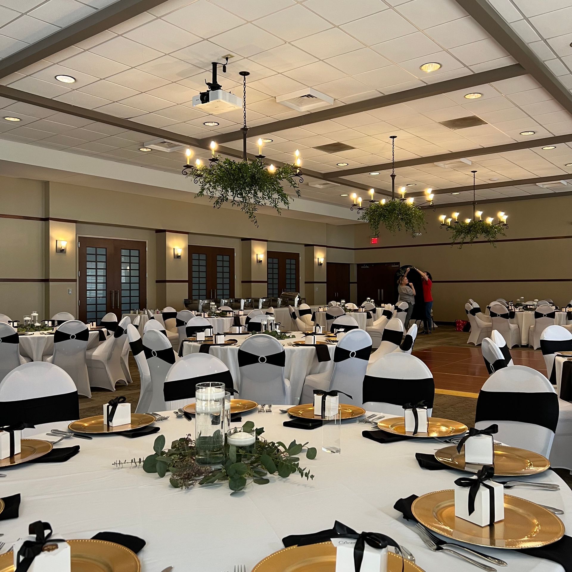 Banquet hall with round tables, white chair covers, and chandeliers before a formal event