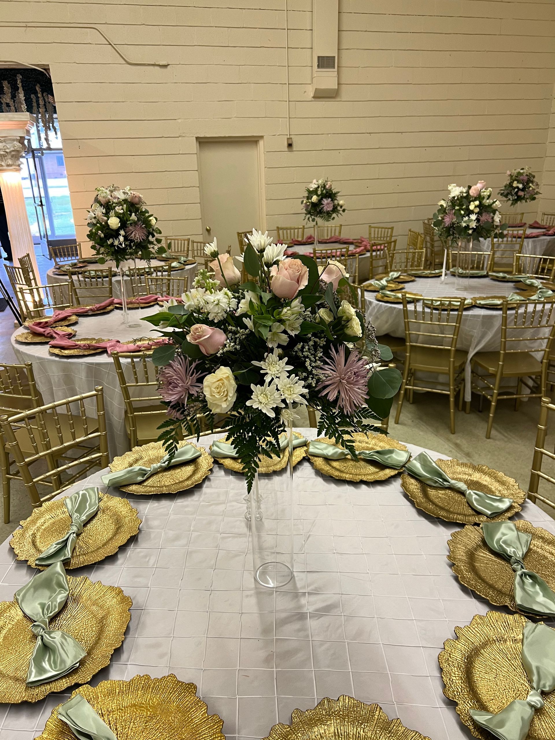Elegant banquet hall with gold-trimmed tables and a large pink-and-white floral centerpiece on the floor