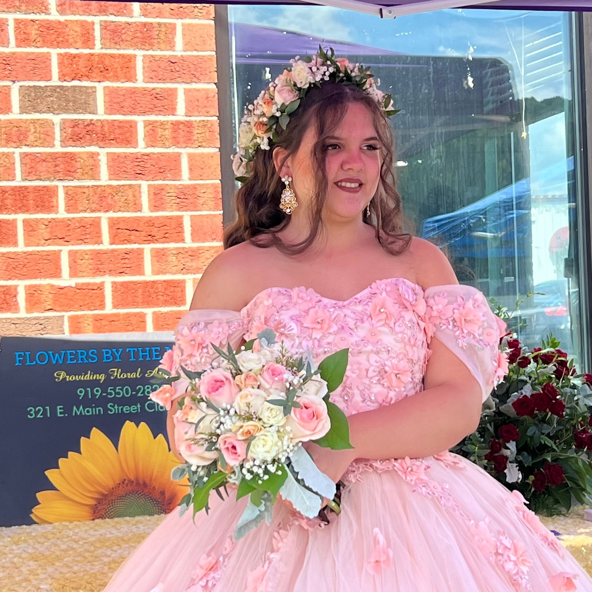 Woman in a pink gown holding a bouquet beside a flower shop window