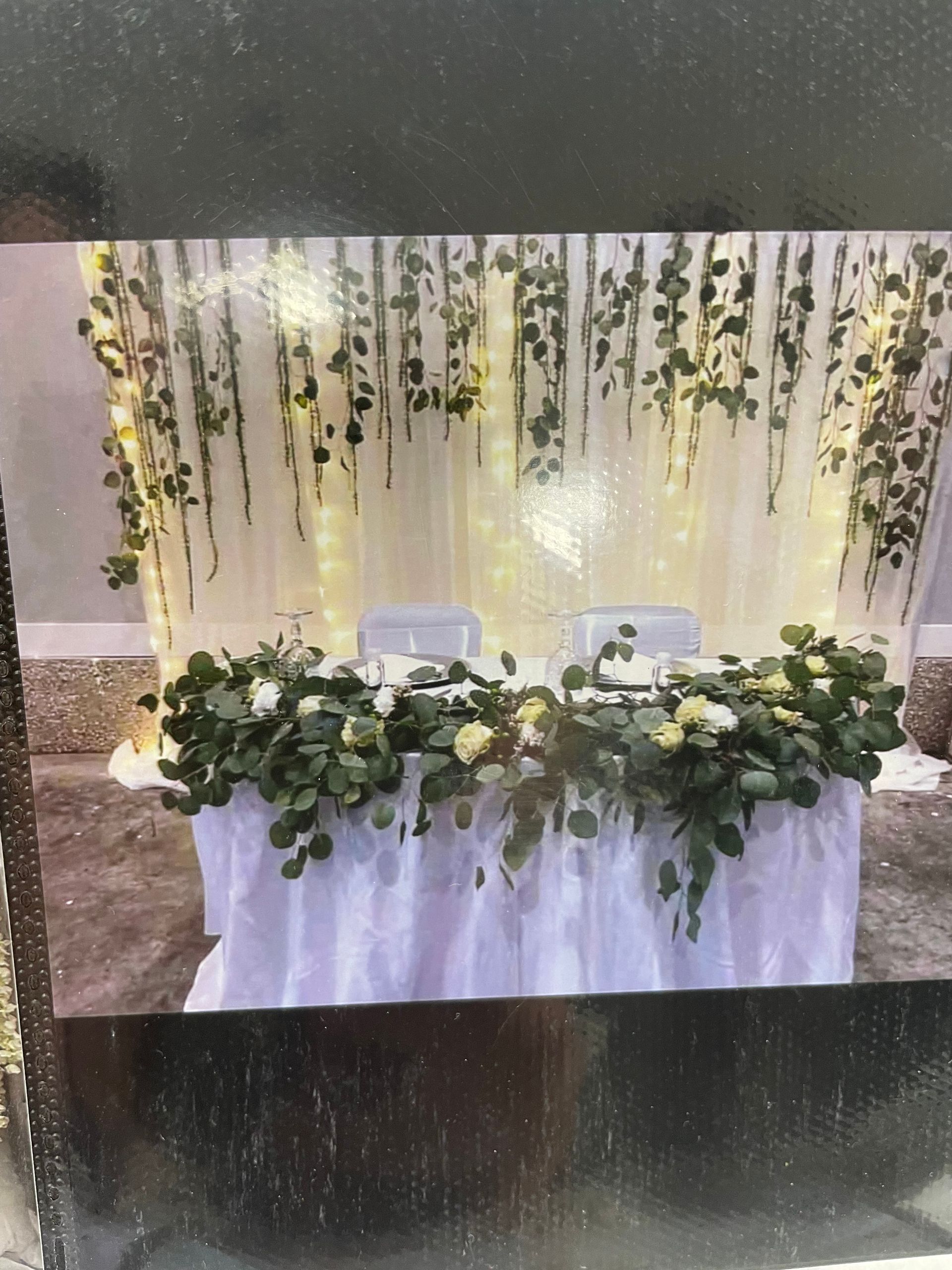 White floral event table with cascading greenery and hanging vines against a soft-lit backdrop