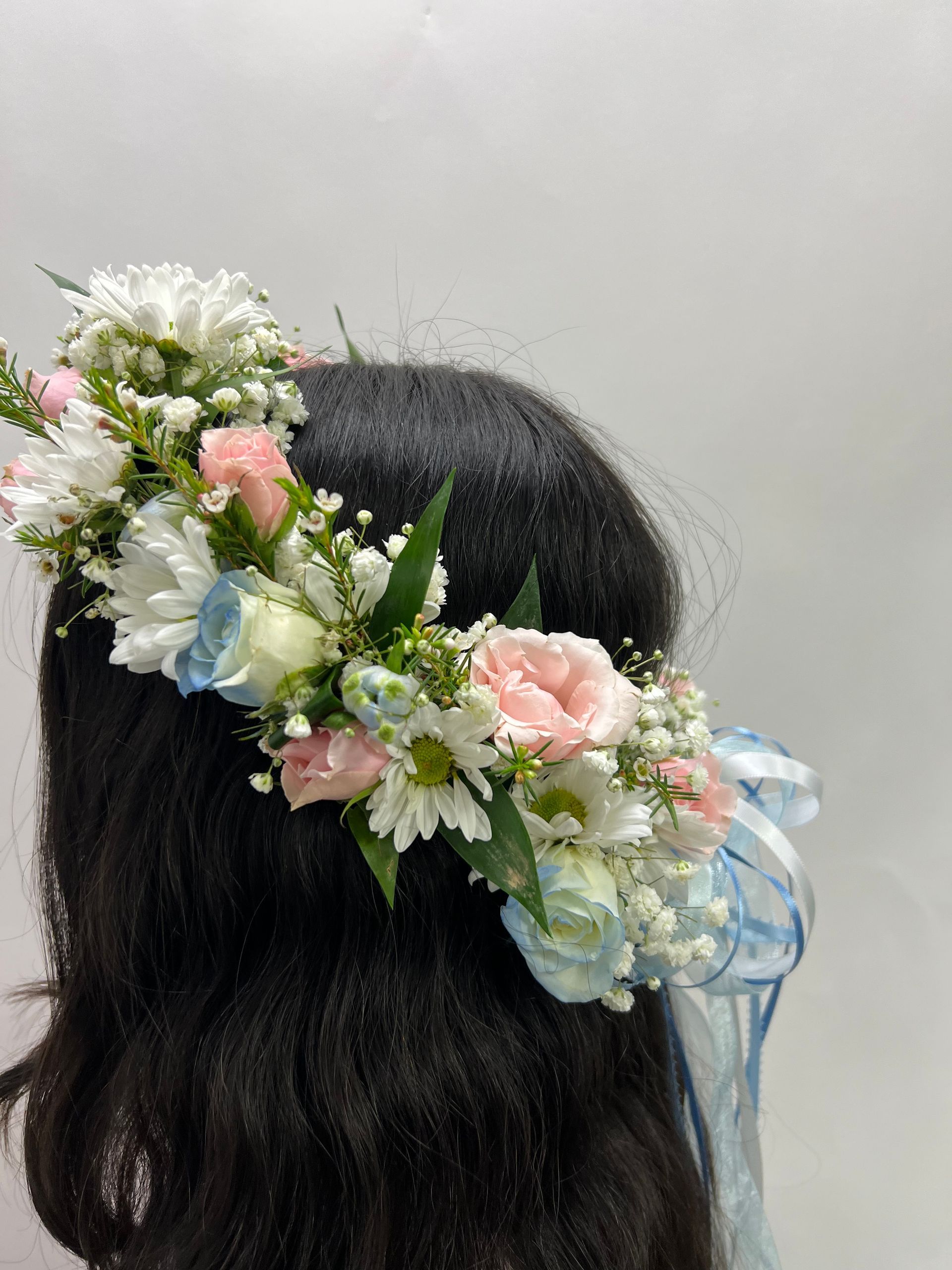 Floral crown with pink, white, and blue flowers worn in dark hair against a light background