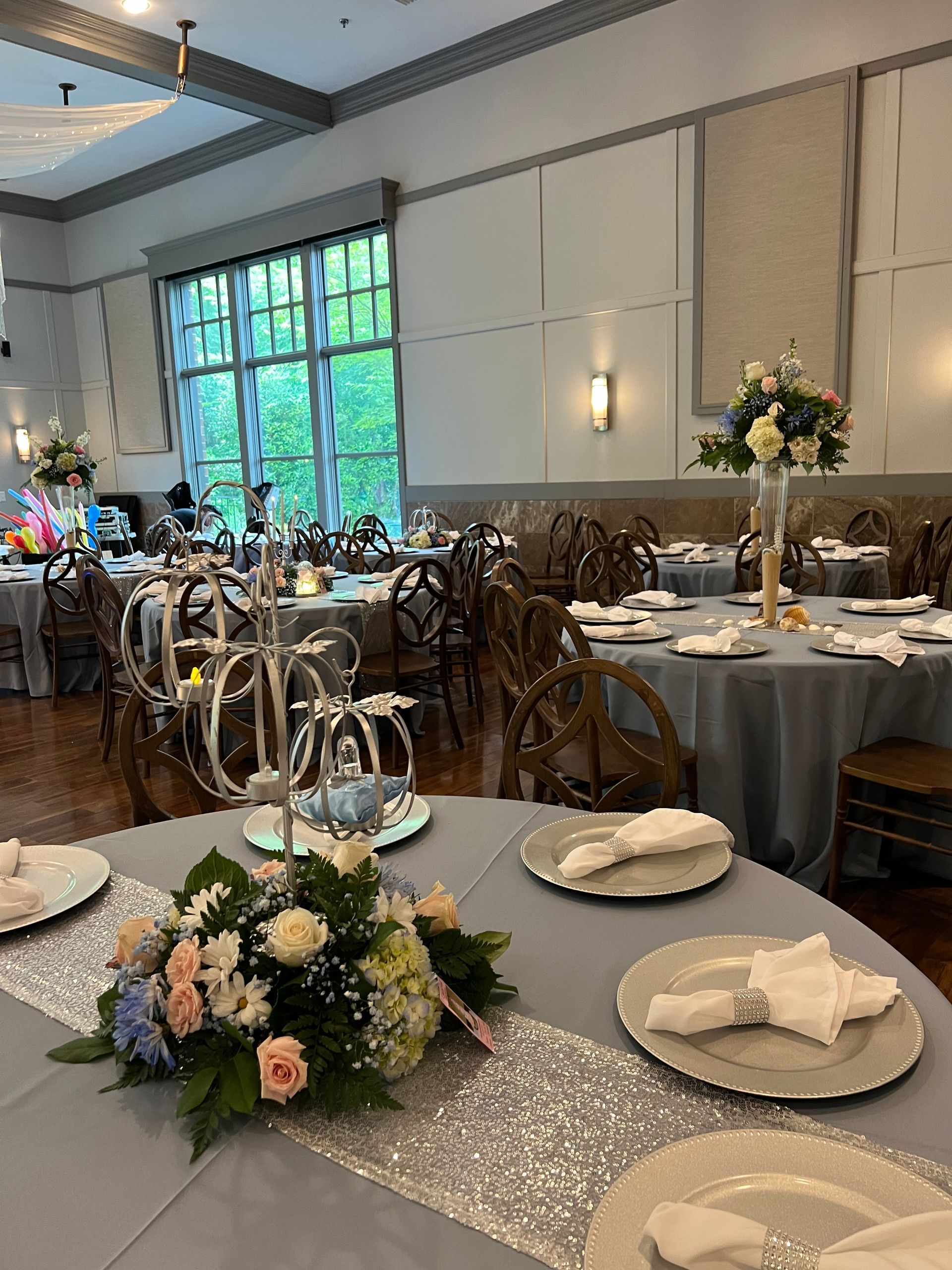 Elegant banquet hall with round tables, floral centerpieces, silver decor, and large windows.