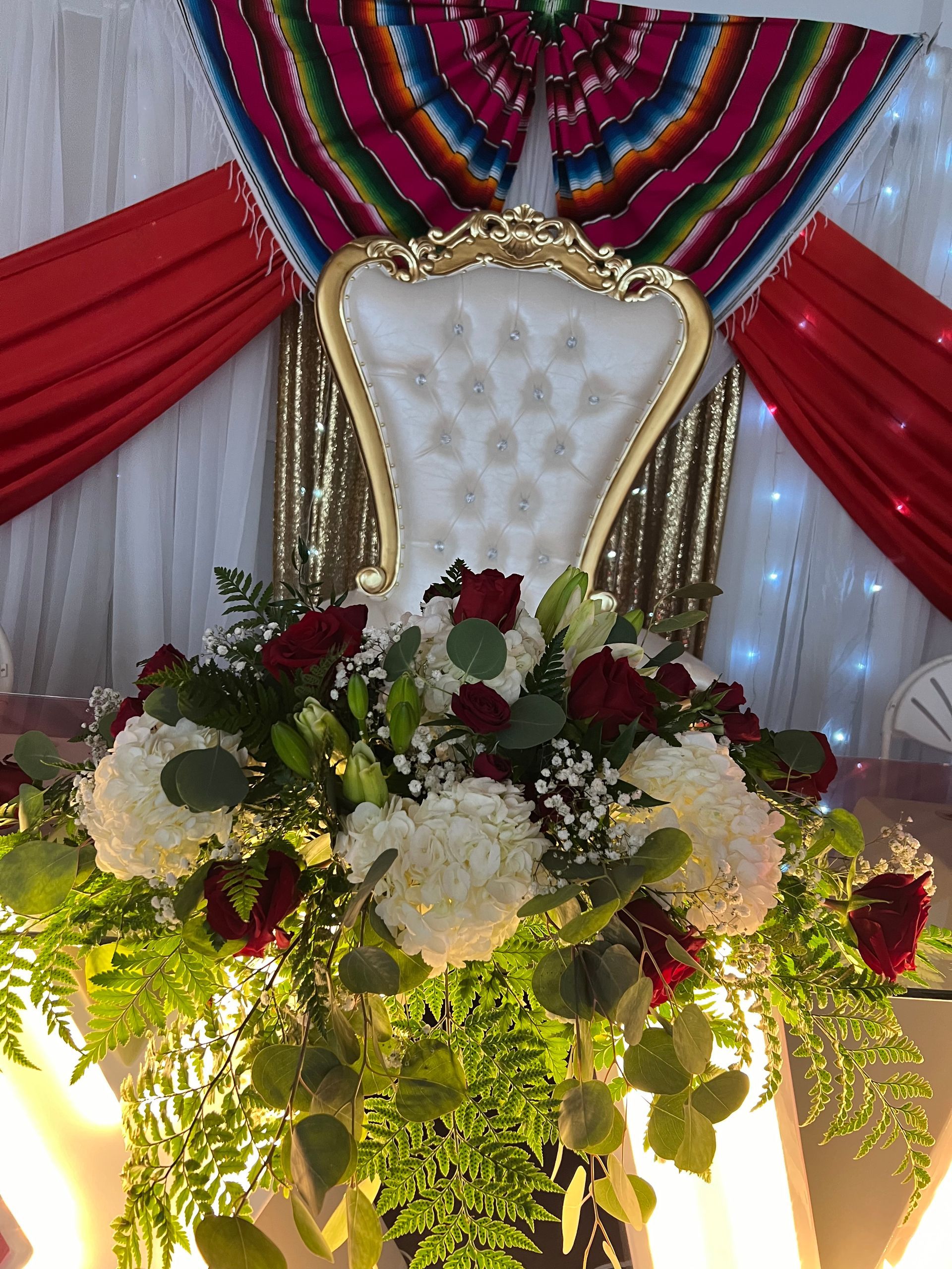 Decorated white chair with floral arrangement and colorful draped fabric backdrop
