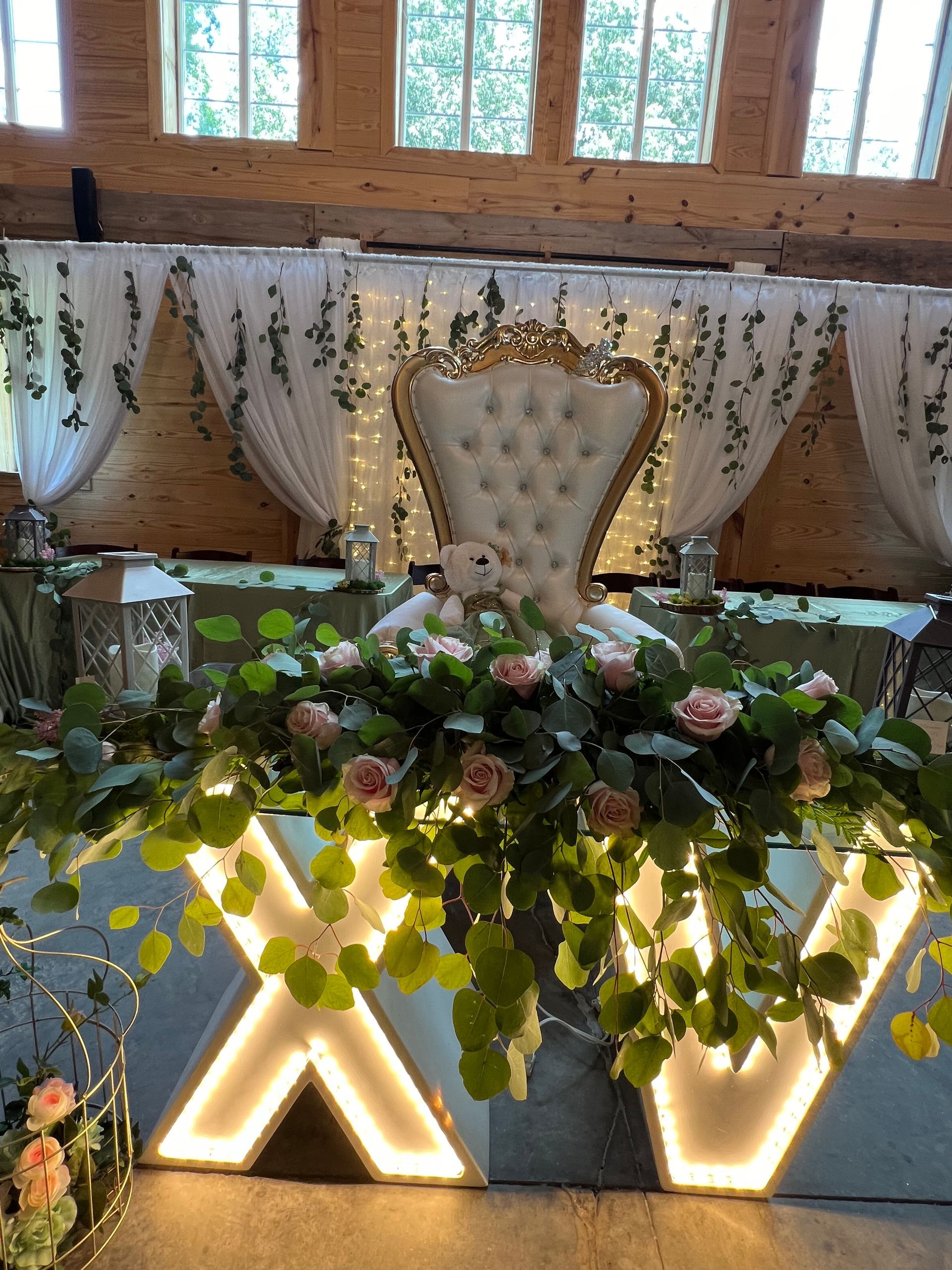Elegant floral wedding stage with a gold throne chair, white drapes, and warm backlit decor.