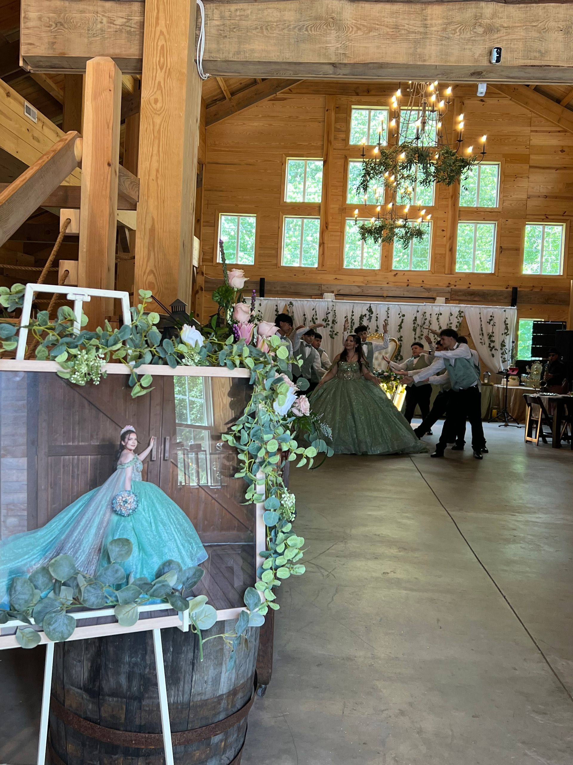 Rustic barn wedding display with teal gown on barrel, floral arch, and tables in the background