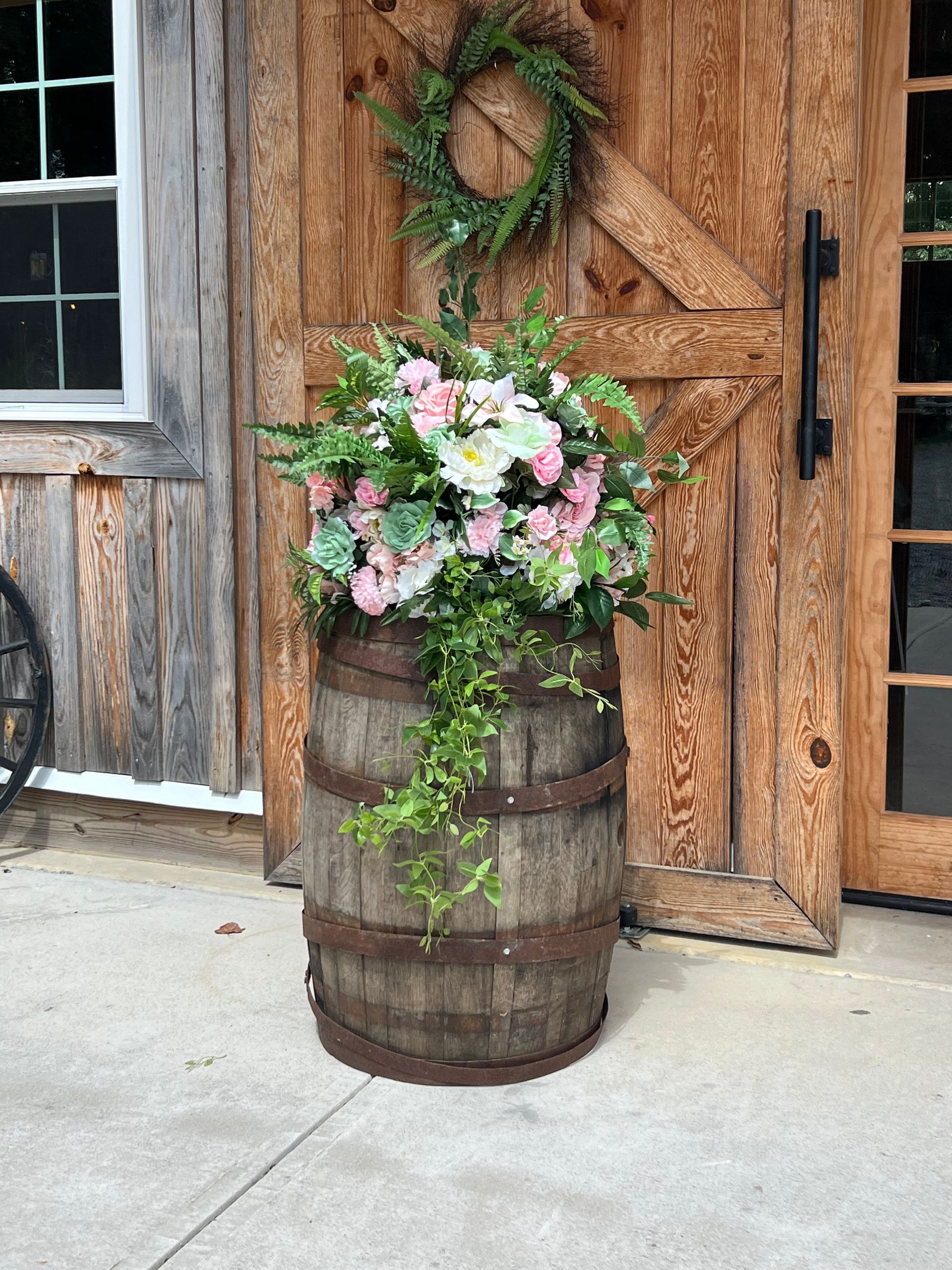 Rustic barrel planter with pink and white flowers beside a wooden door and wreath