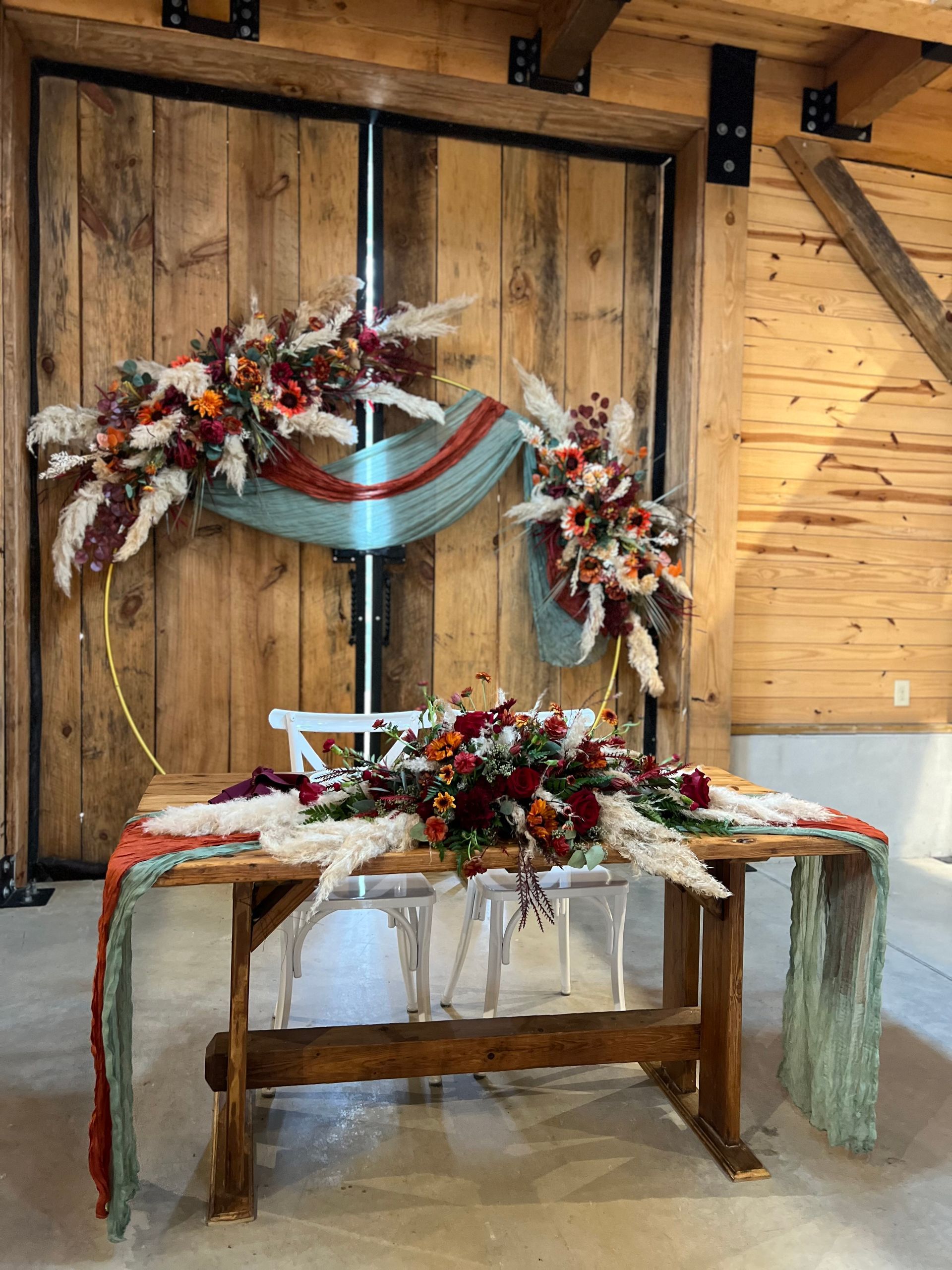 Rustic wedding arch and decorated table with fall flowers and draped fabric in a wooden barn setting