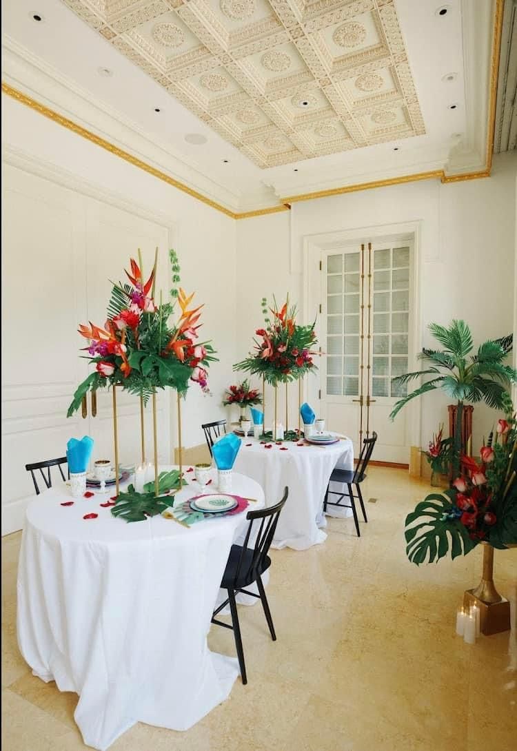 Elegant dining room with white-clothed tables and tall red-and-green floral centerpieces