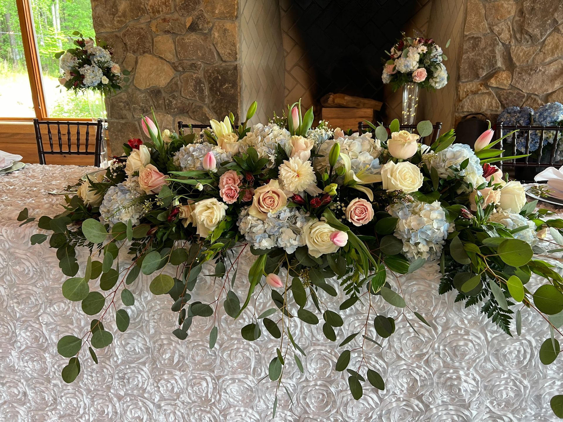 White and blush floral arrangement with greenery on a table in a rustic stone venue