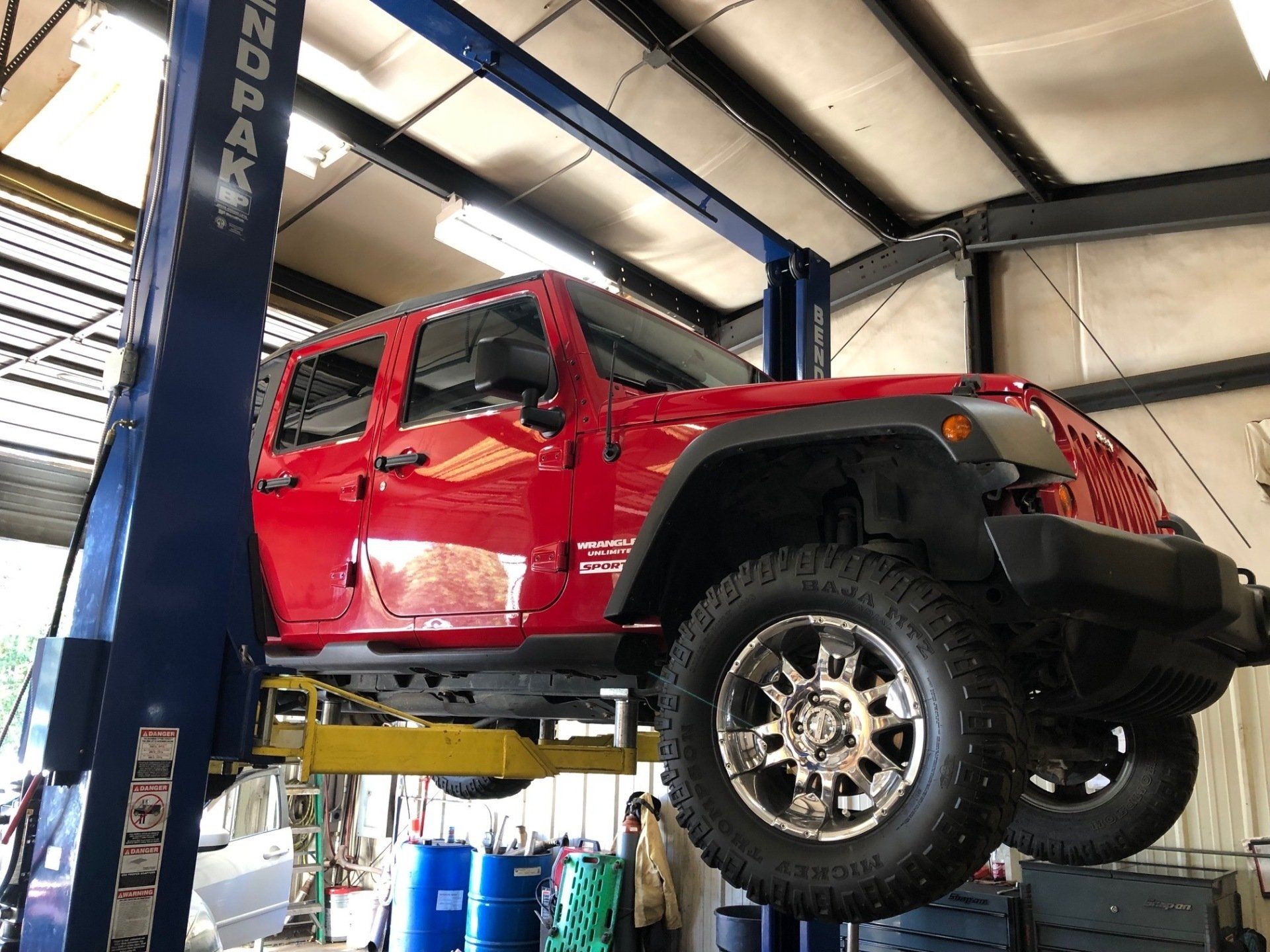 A red jeep is sitting on a lift in a garage.