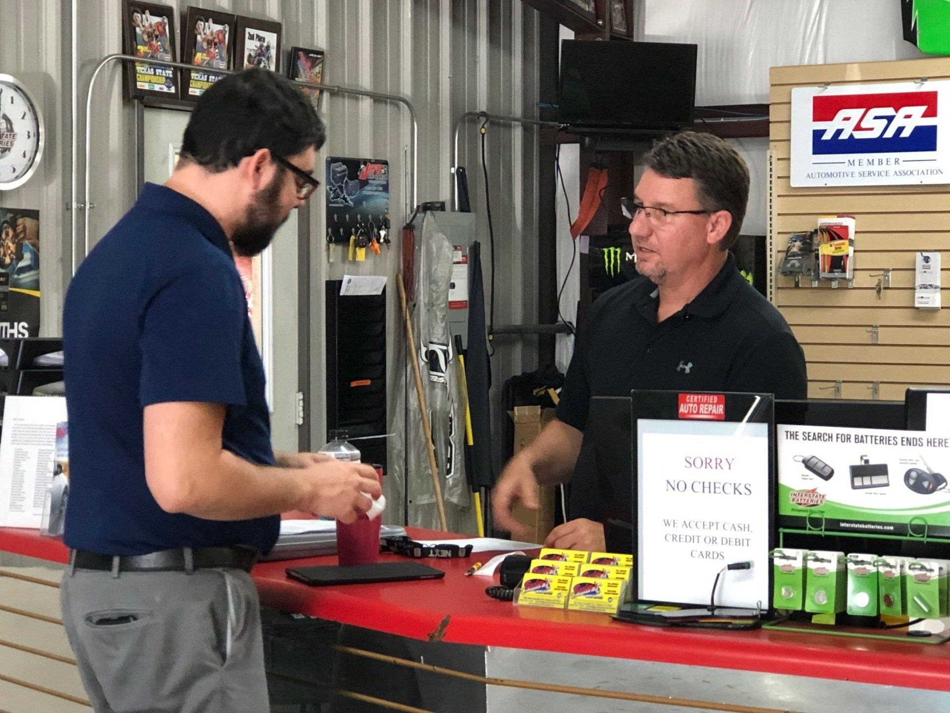 Two men are standing at a counter in a store talking to each other.