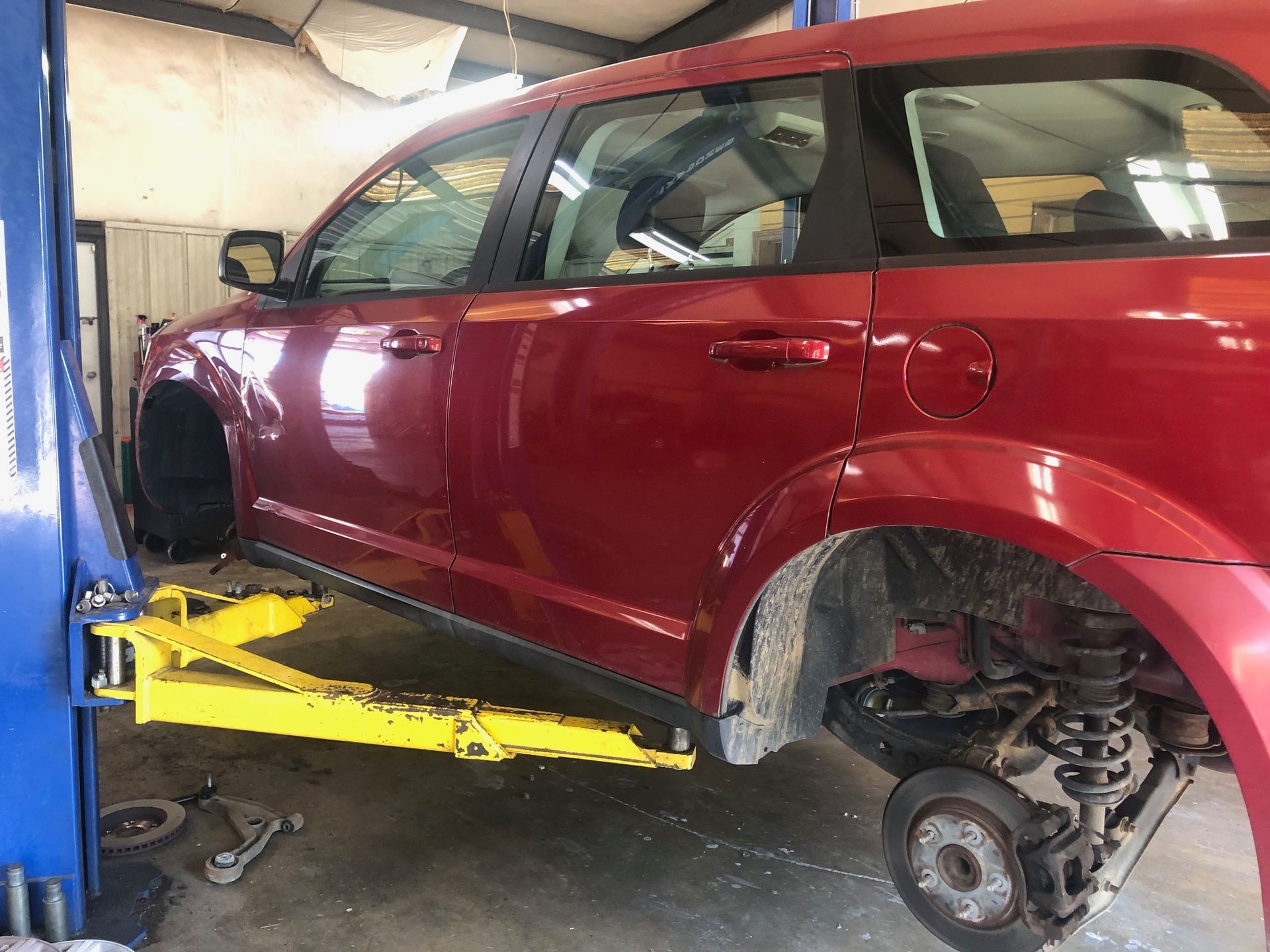 A red dodge journey is sitting on a lift in a garage.
