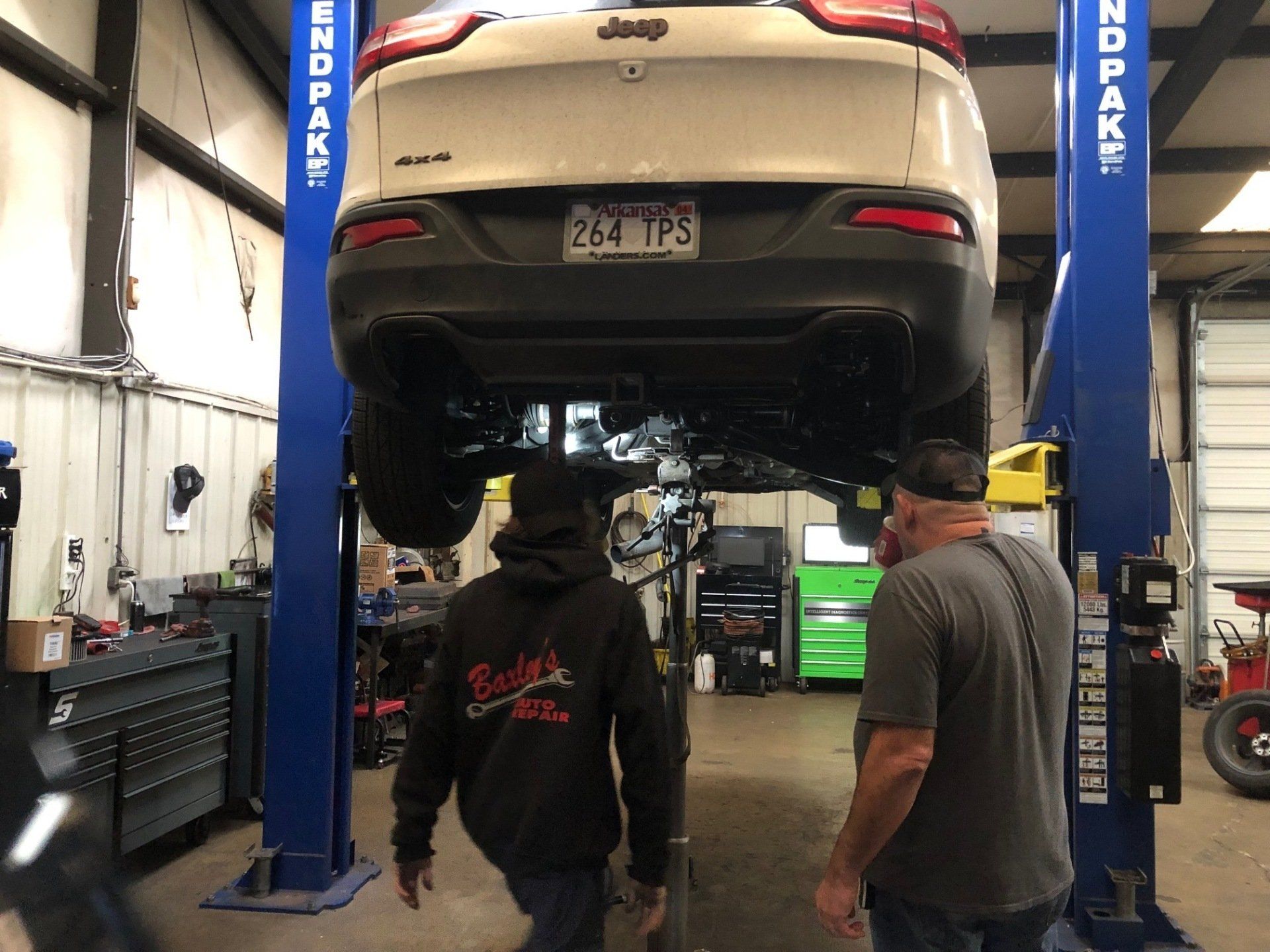 Two men are looking at a jeep on a lift in a garage.