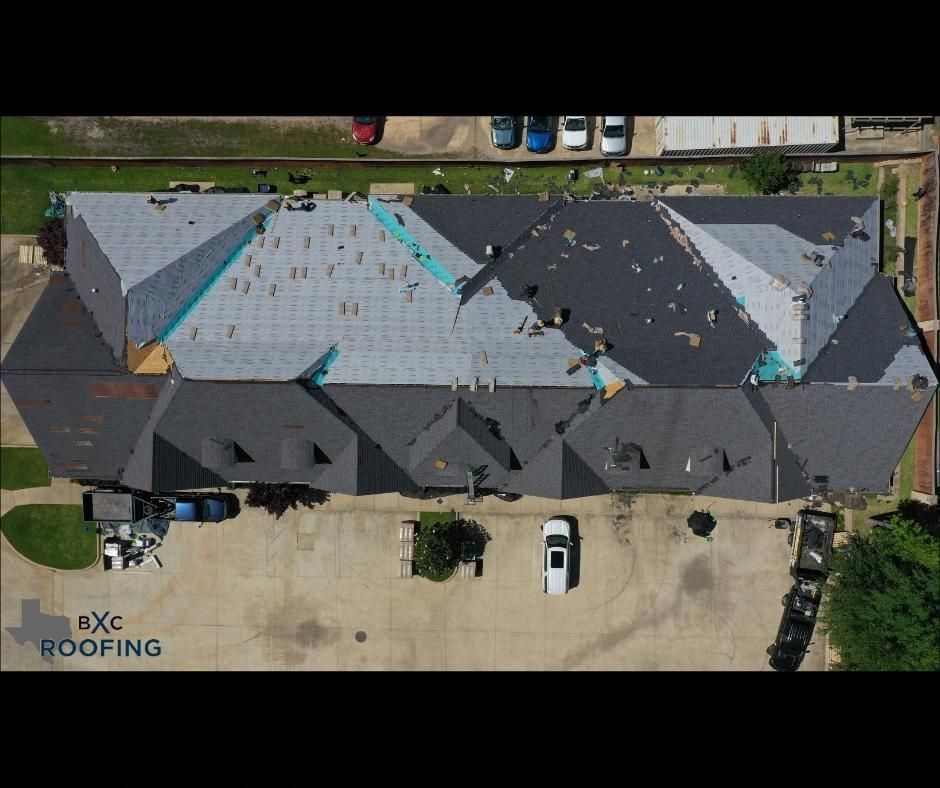 Aerial view of a roof under repair with torn shingles, gray tarp, and roofing workers on a residential building.