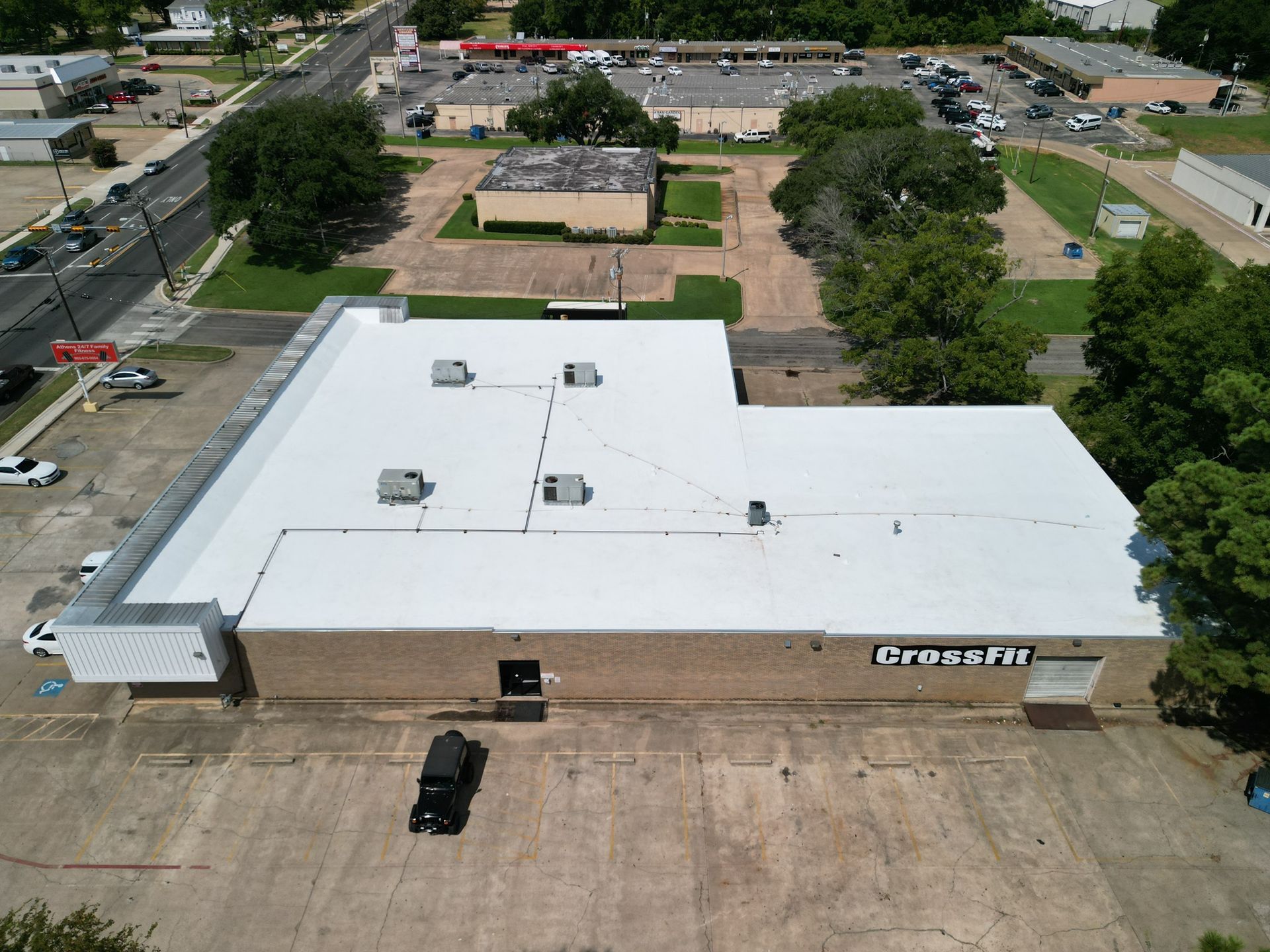 Aerial view of a large white-roofed commercial building with a parking lot and surrounding trees.