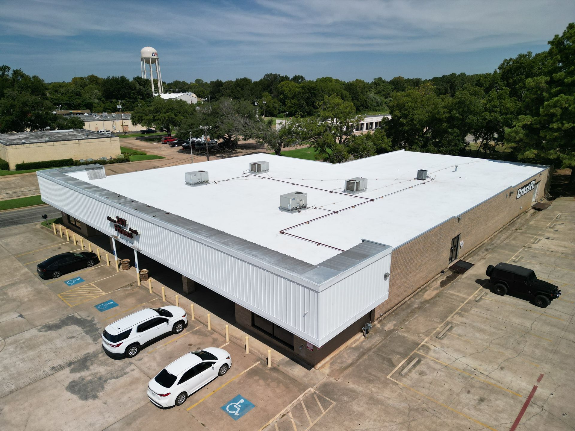 Aerial view of a white-roofed commercial building with parked cars and trees around it.