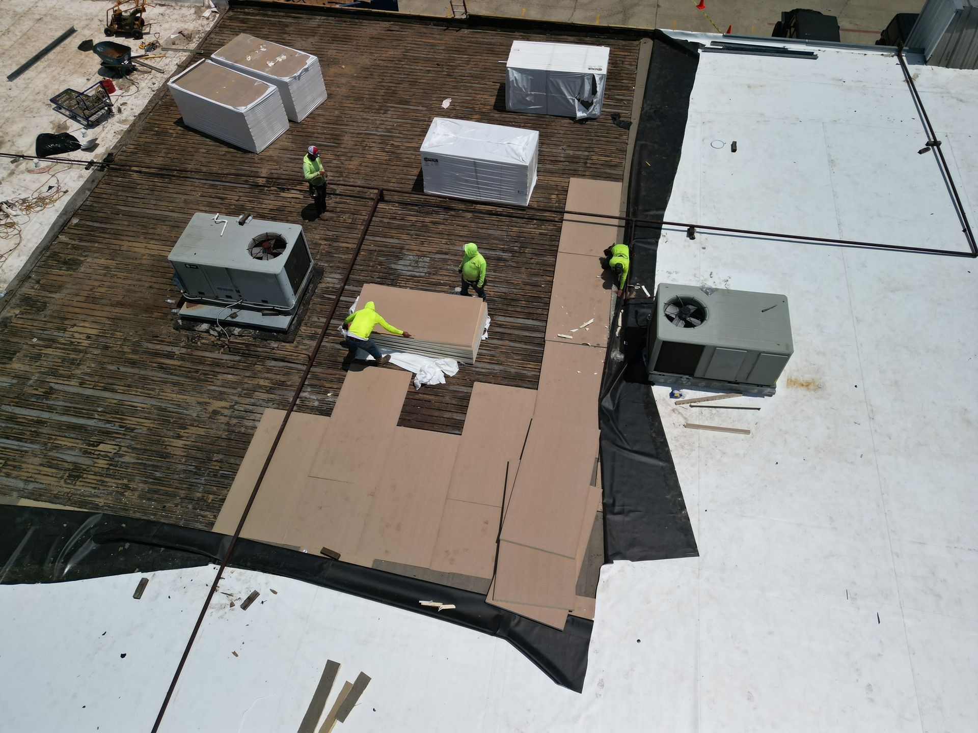 Rooftop worksite with workers, HVAC units, and stacked materials on a flat roof