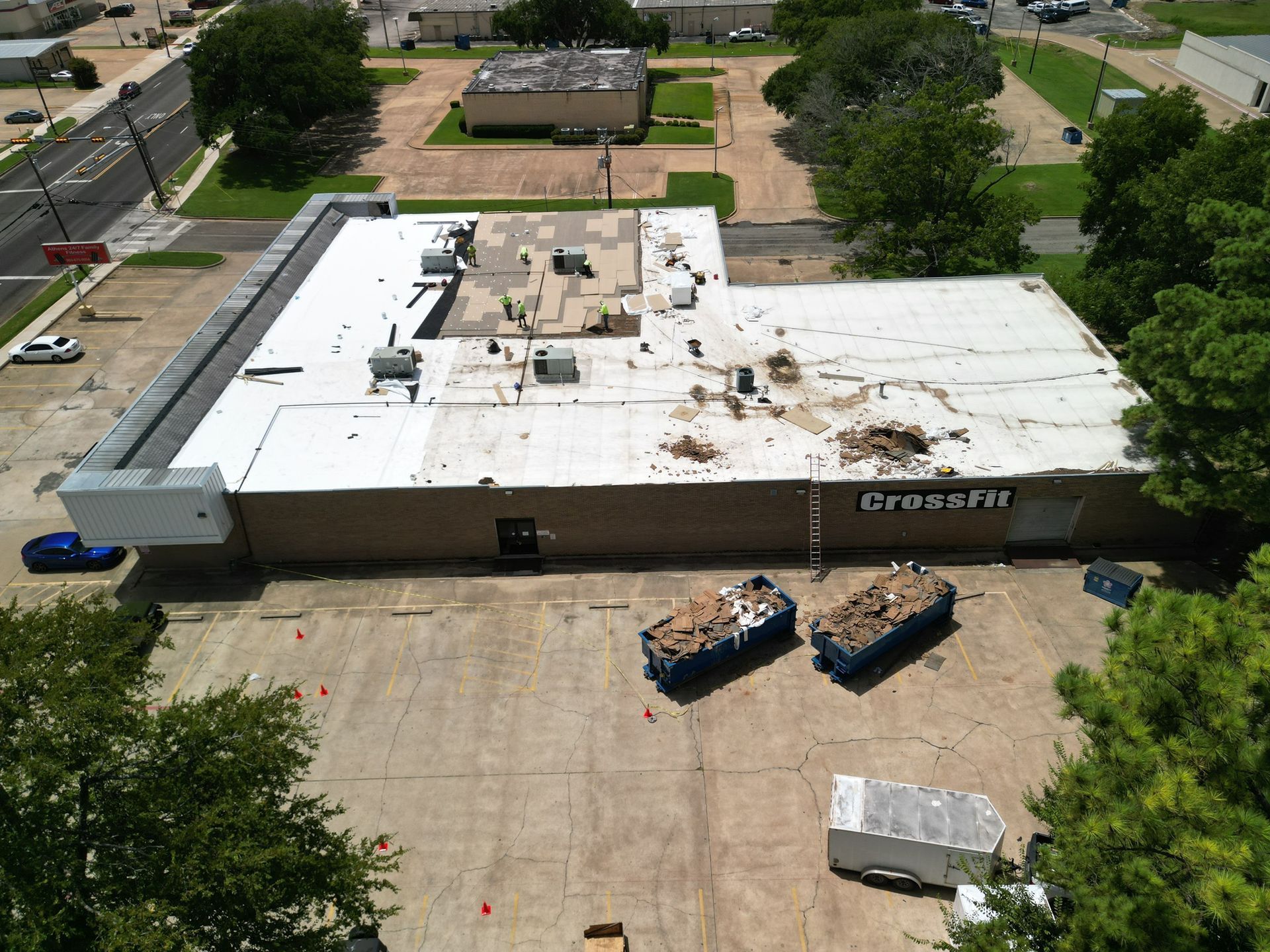 Aerial view of a white-roofed commercial building with construction equipment in a parking lot and trees nearby