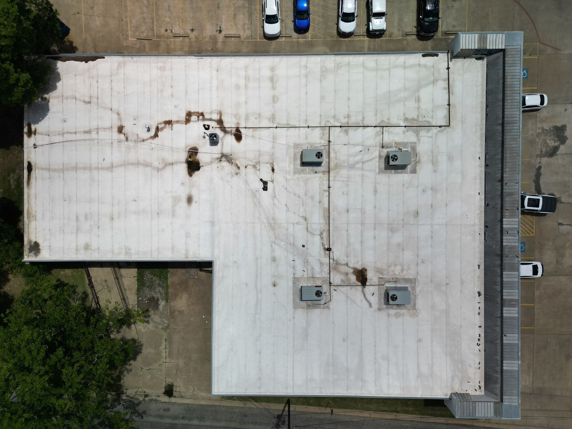 Aerial view of a flat white-roofed building with parked cars along the top and right edges.