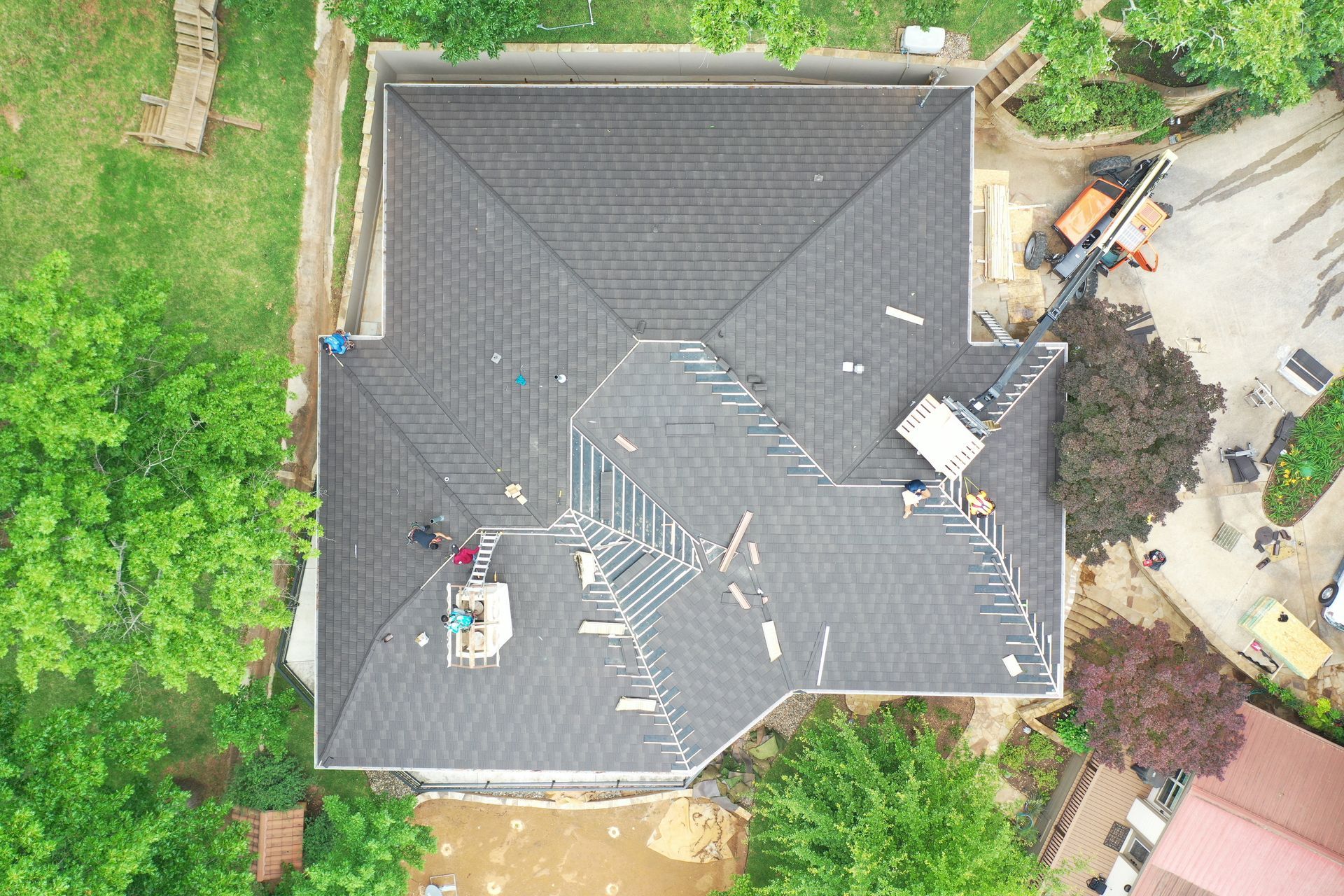 Aerial view of a house with a dark gray roof surrounded by trees and a driveway with construction equipment.
