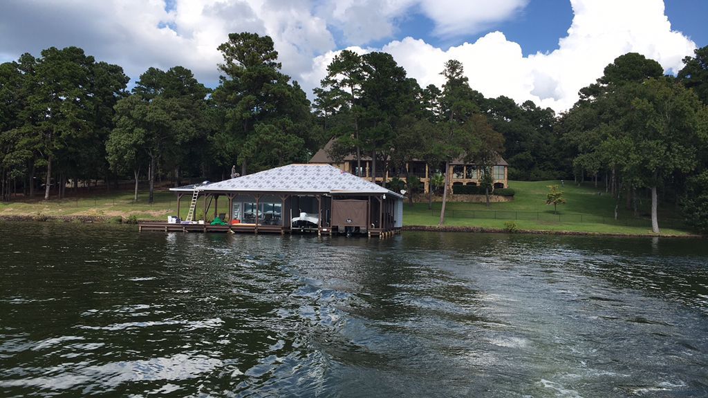 Lakeside dock with a small boathouse, boats, and trees on a calm waterfront under a cloudy sky